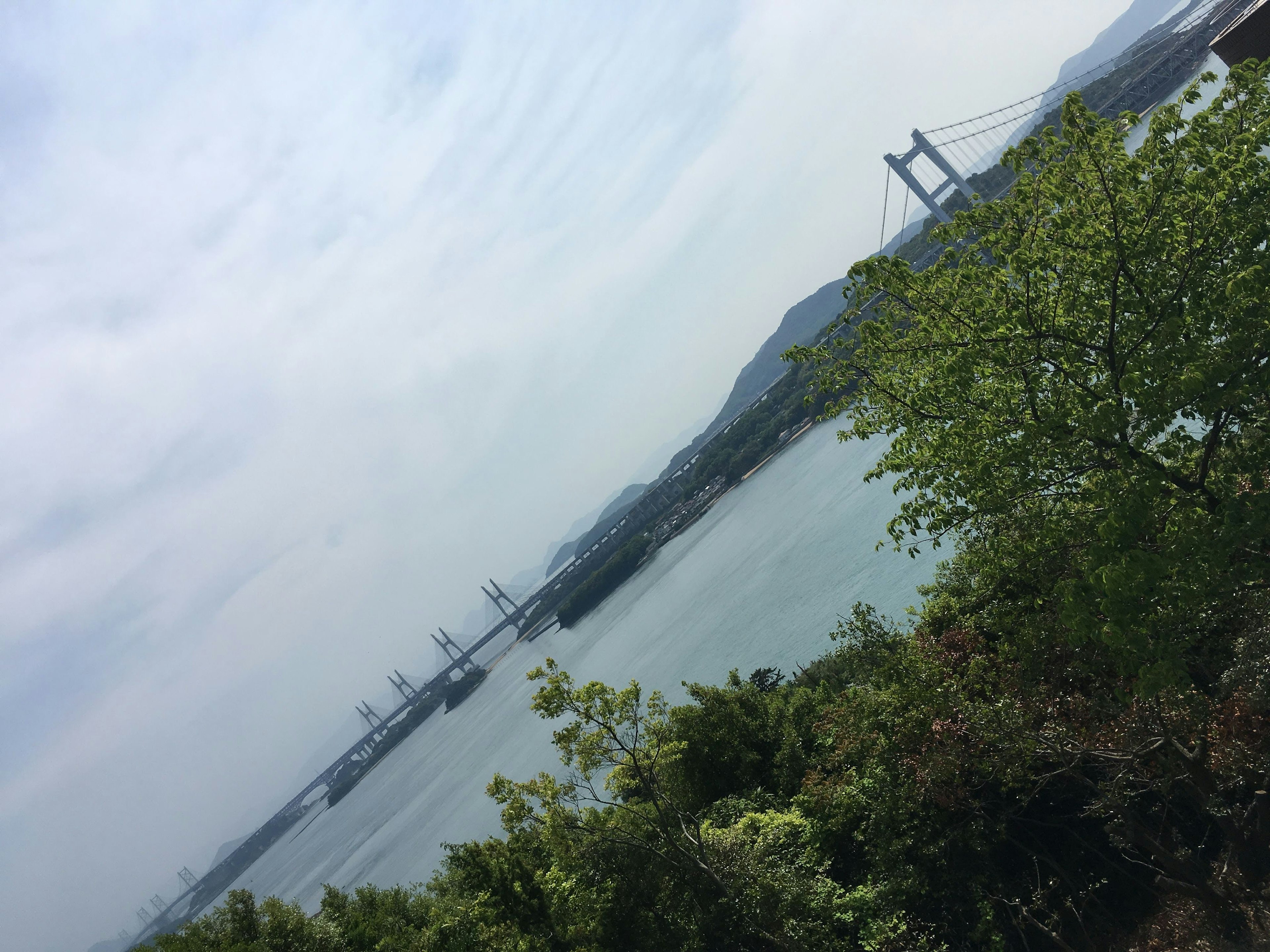 Malersicher Blick auf Wasser und Brücke mit grünem Laub und bewölktem Himmel