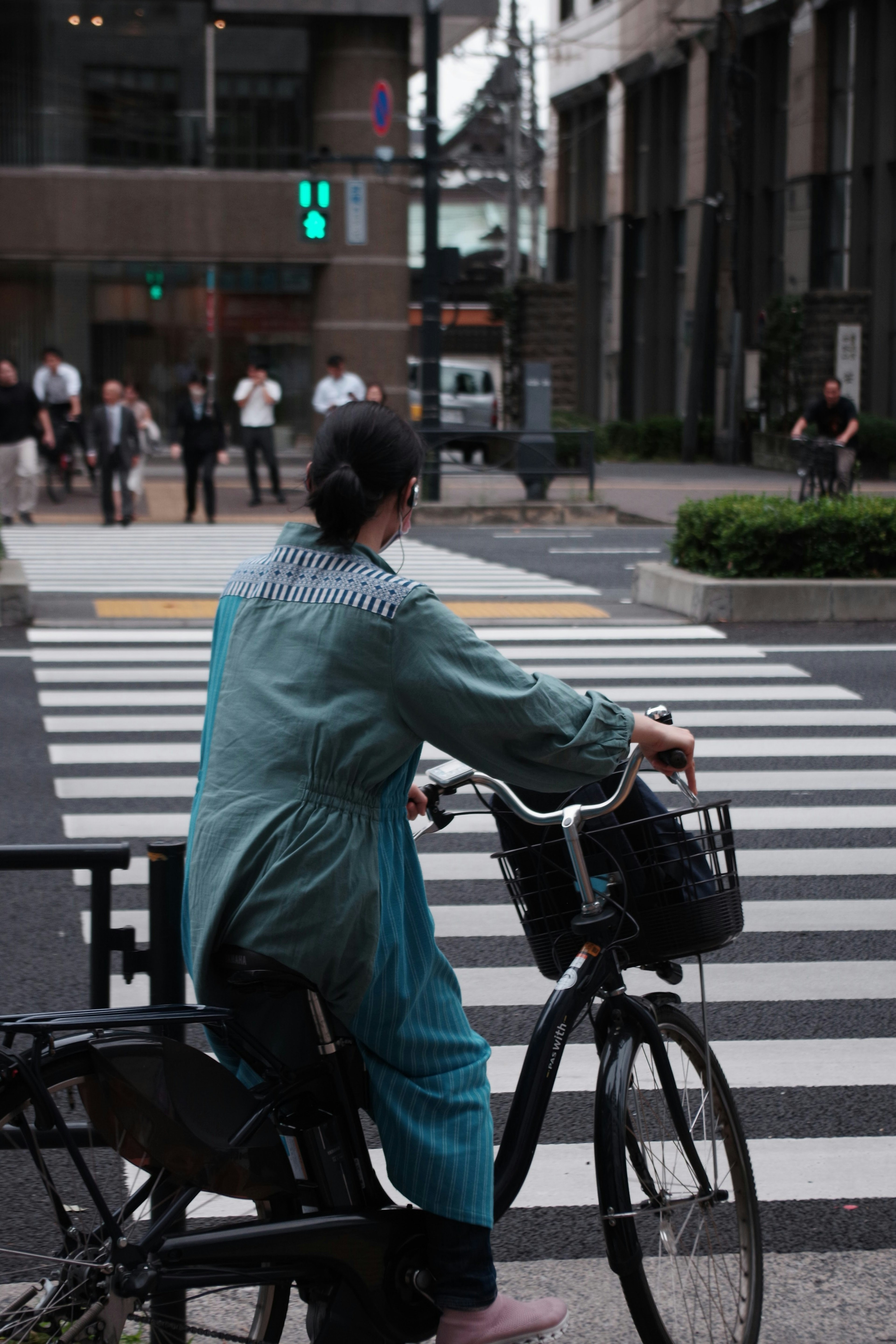 青い服を着た女性が自転車に乗り、交差点で信号を待っている