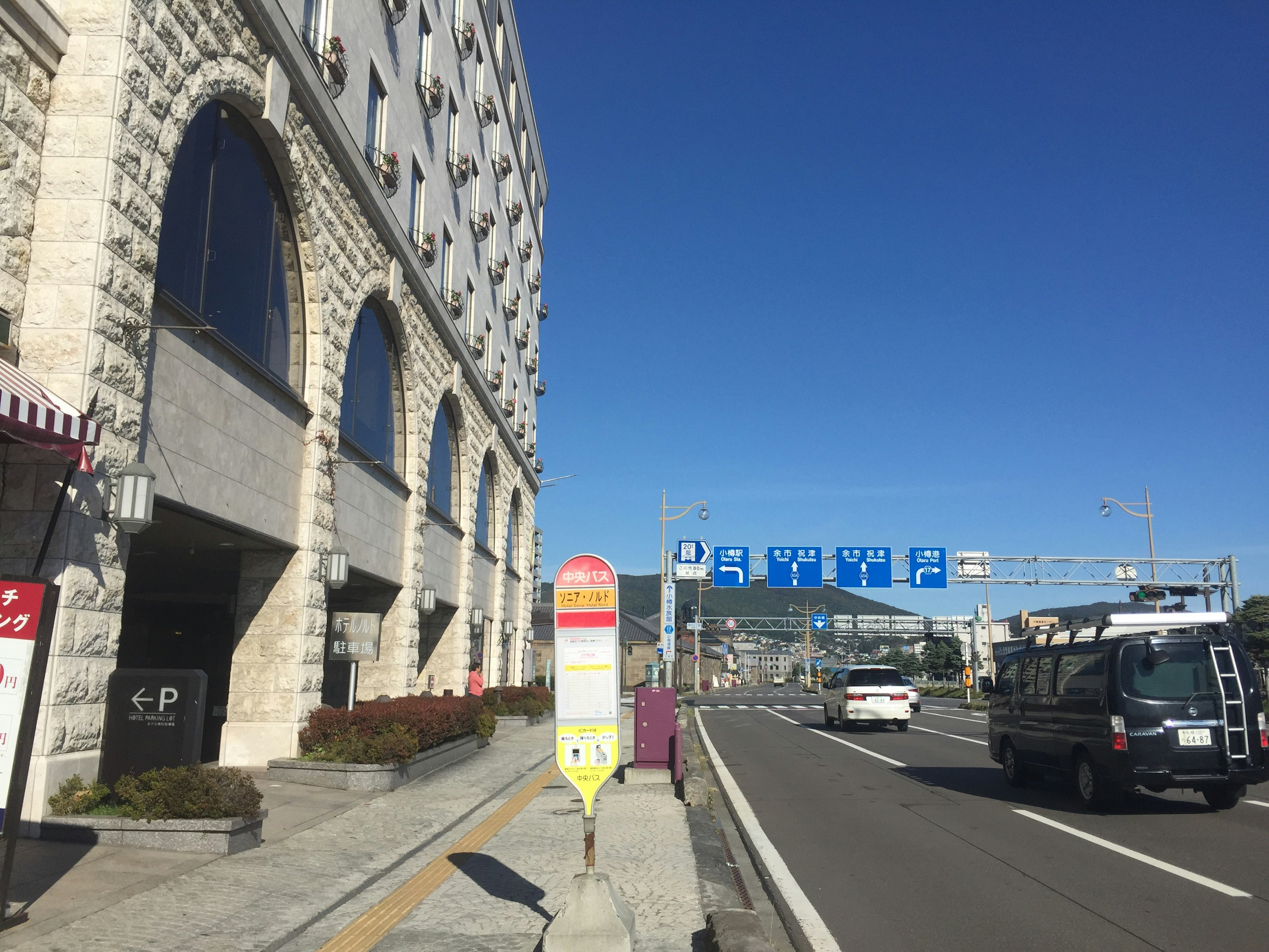 青空の下にある石造りの建物とバス停が見える風景