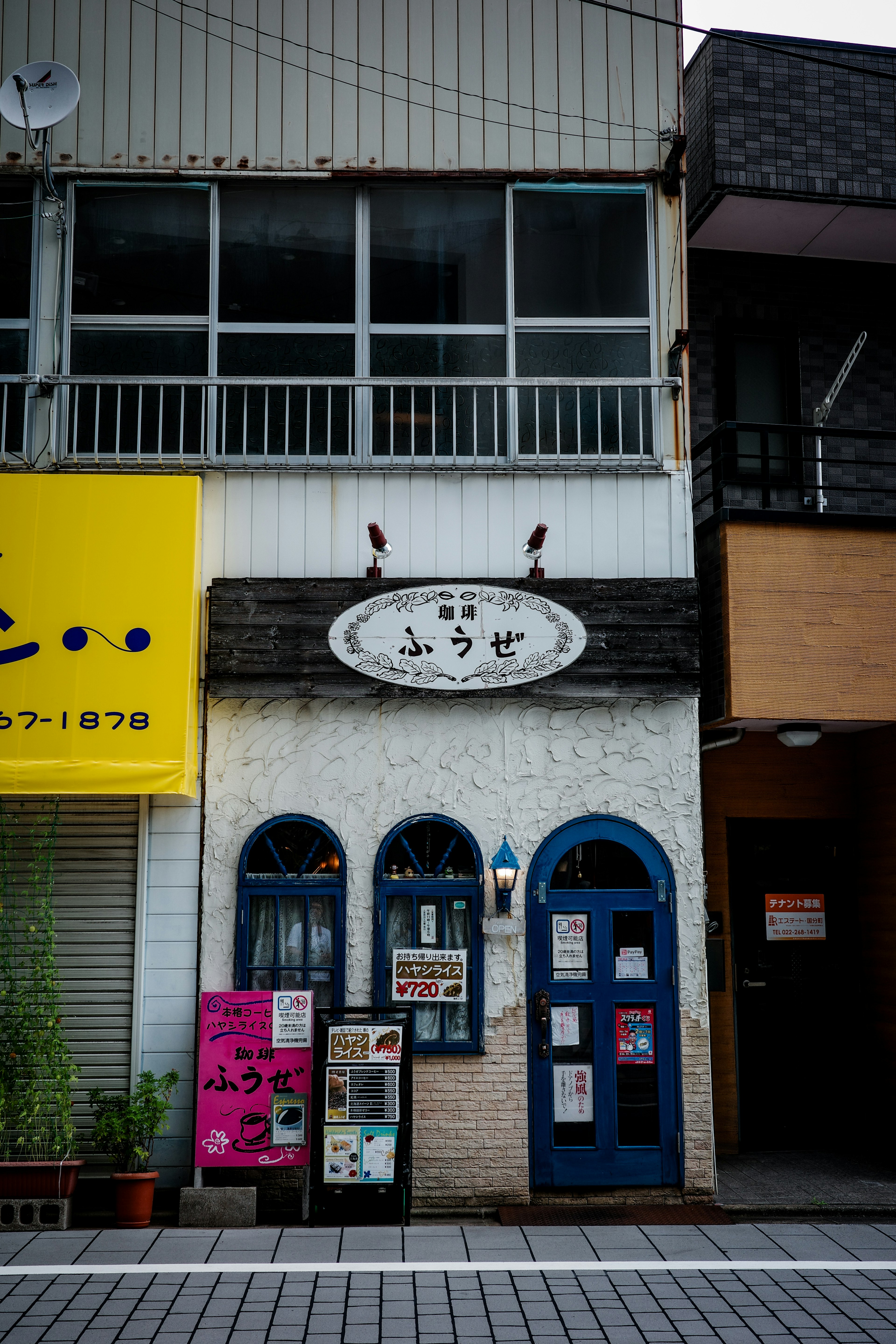 Fassade eines Cafés mit blauen Türen weißen Wänden und einem Schild