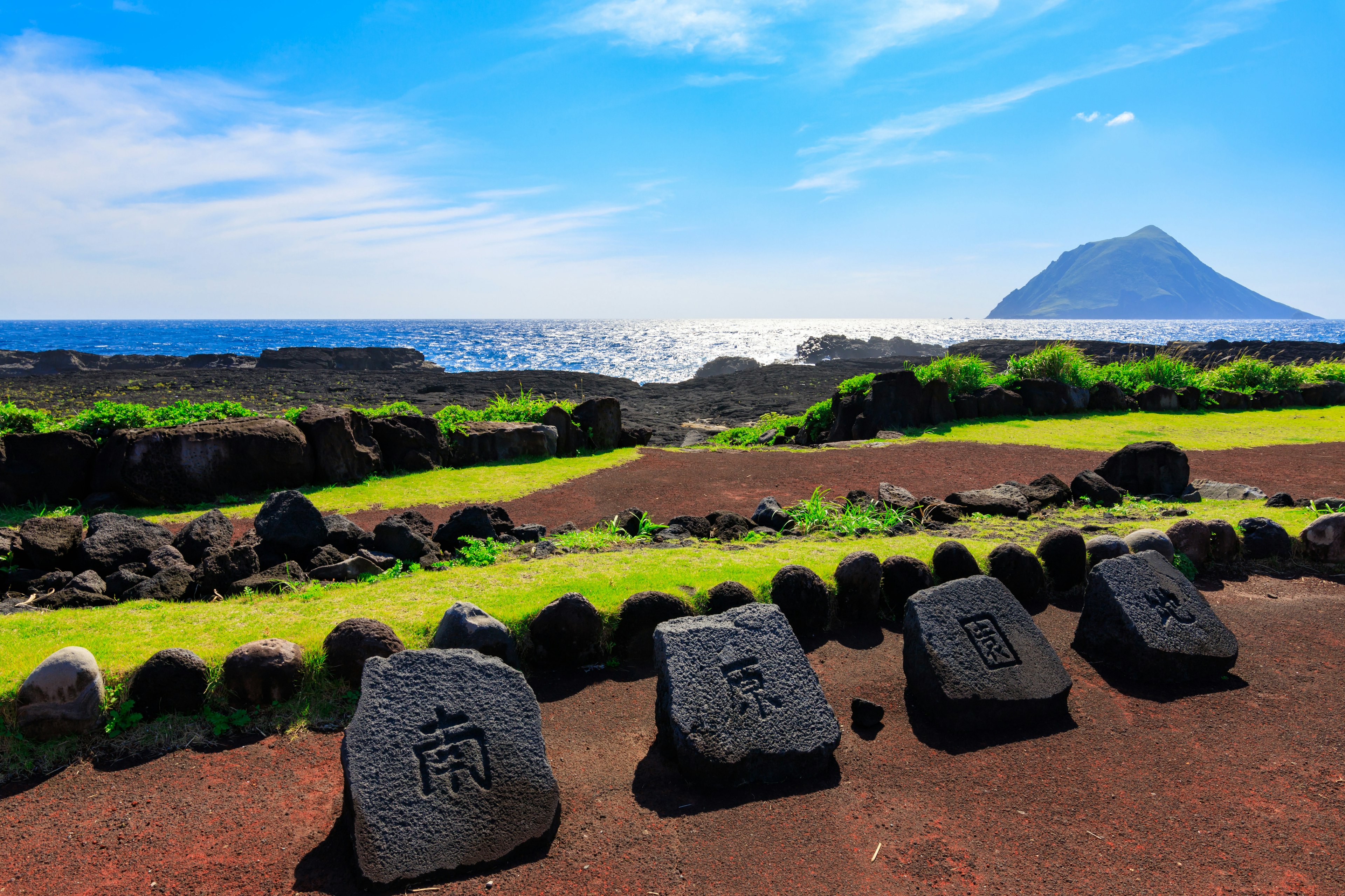 Un grupo de monumentos de piedra negra con inscripciones contra un fondo de mar y cielo azul