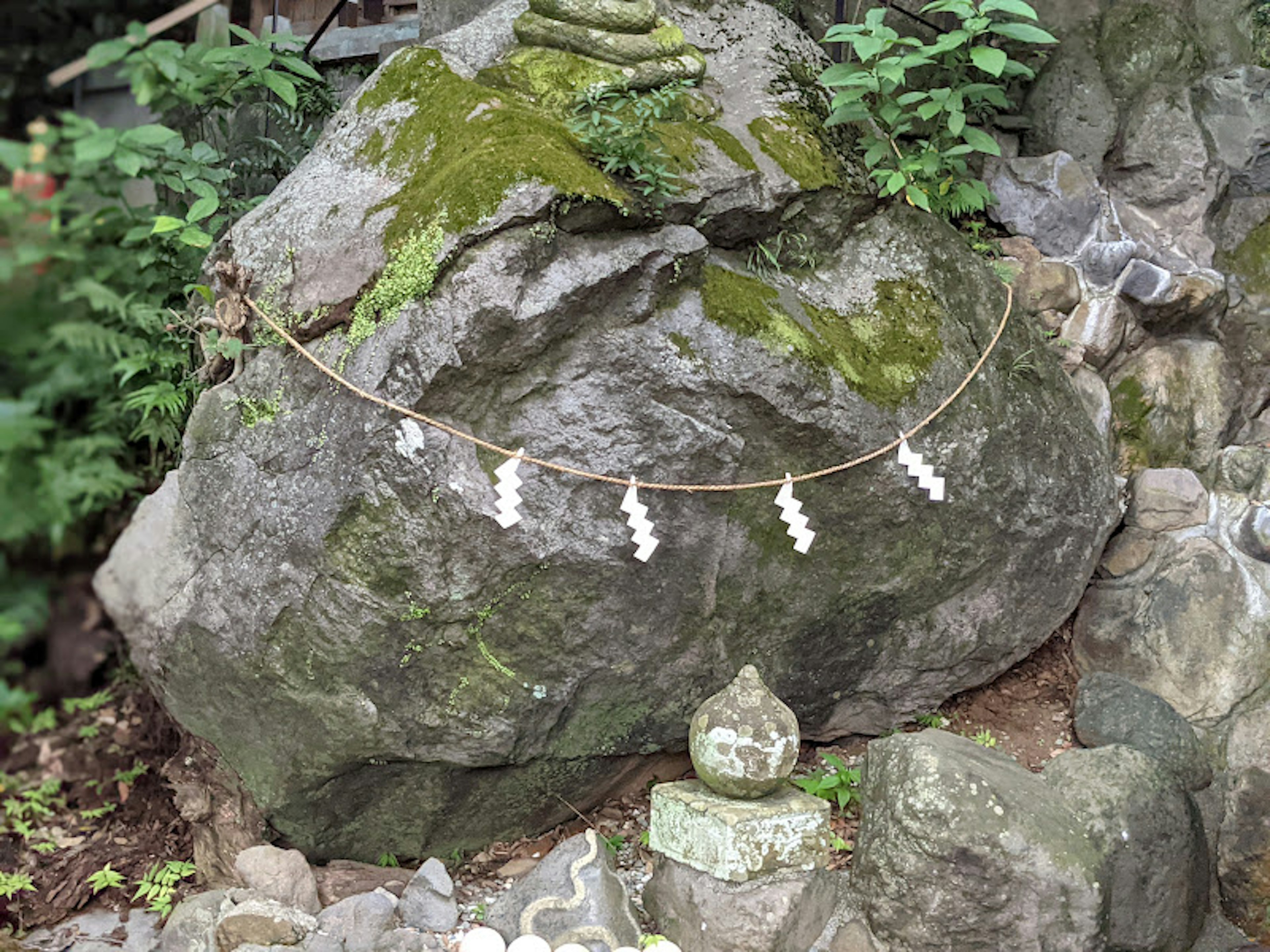 Una gran roca cubierta de musgo con elementos decorativos blancos colgando de una cuerda