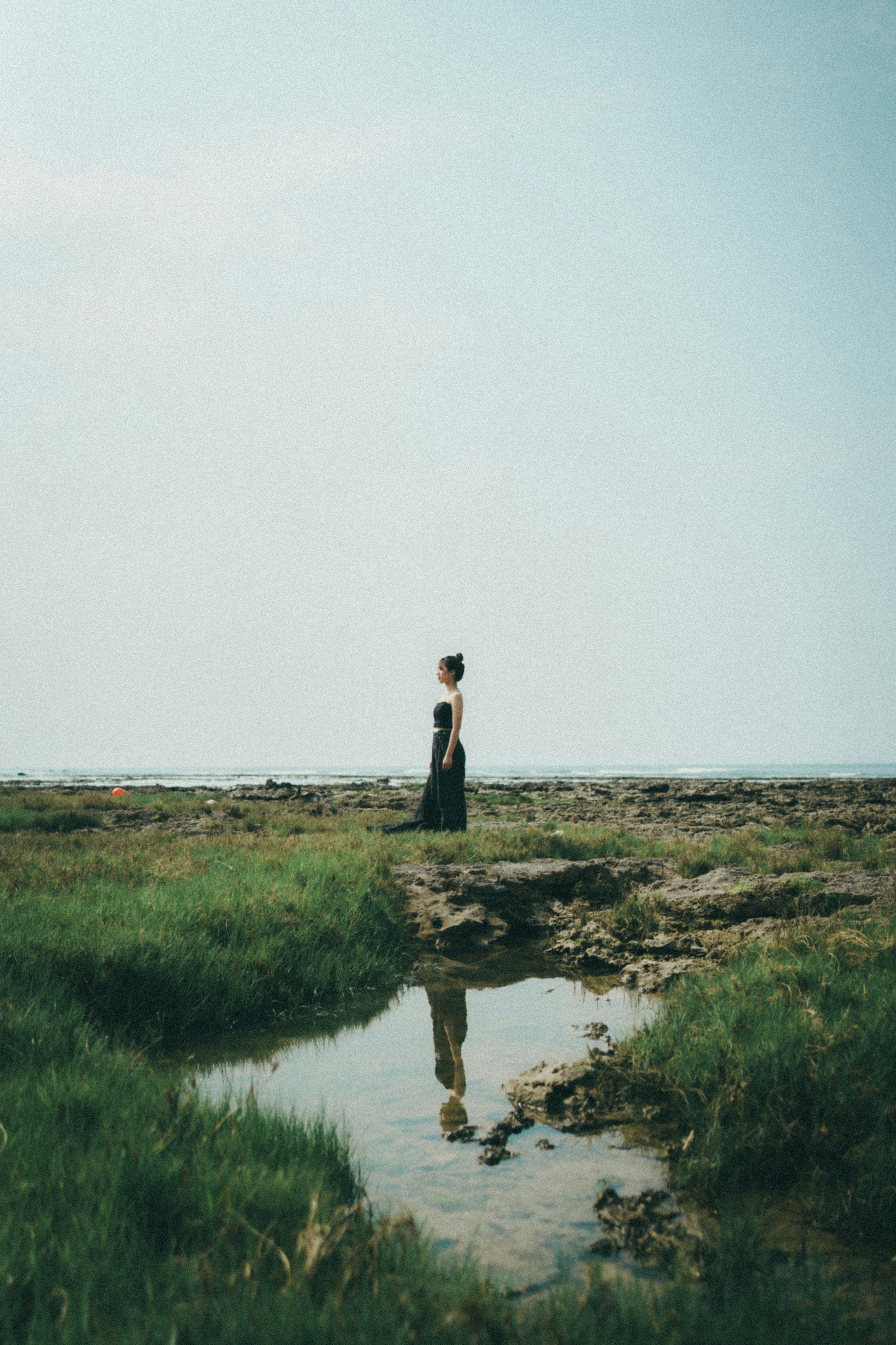 A woman standing quietly under a wide sky with a serene landscape