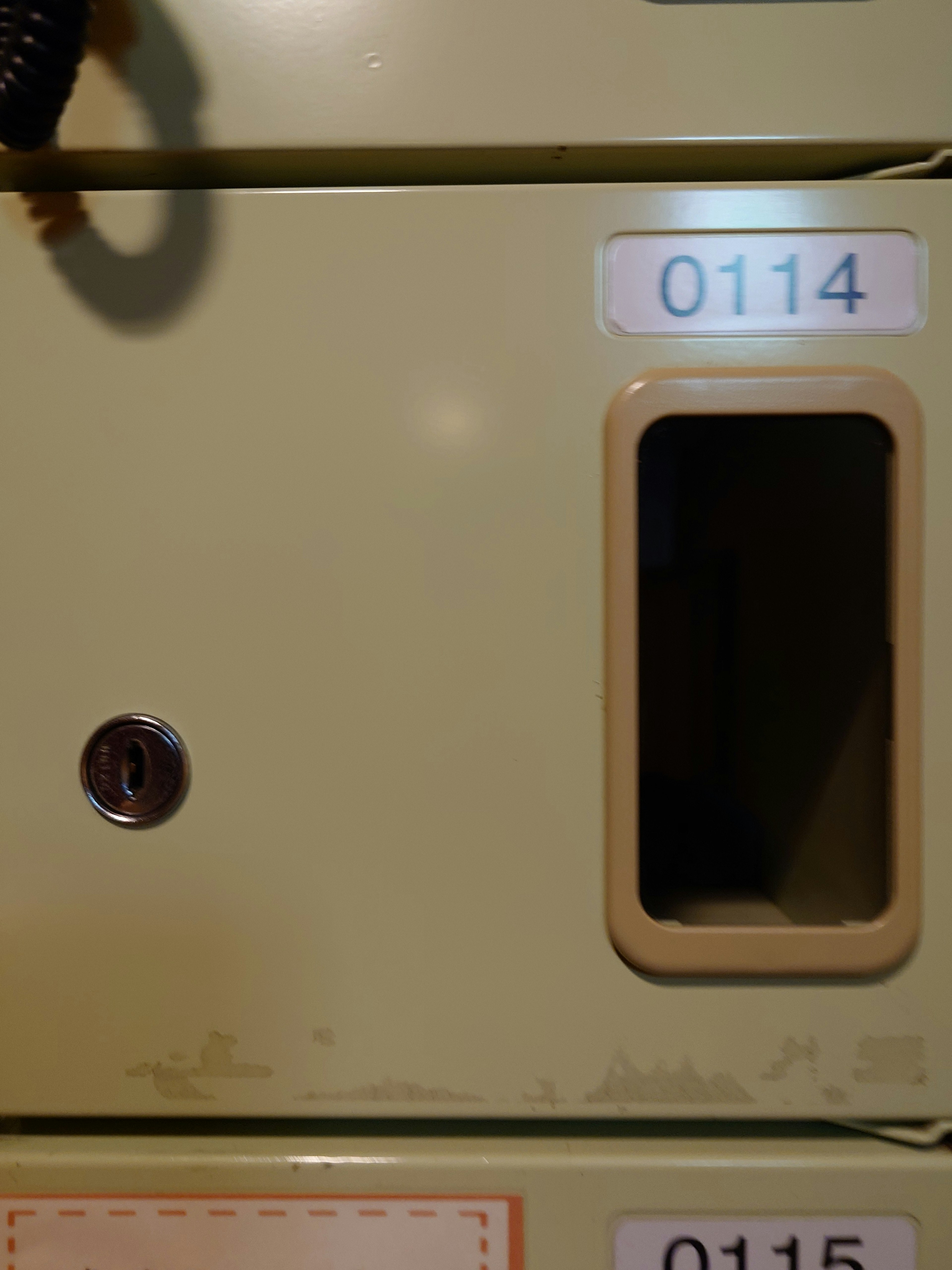 A section of a green locker featuring a keyhole and a small window with the number 0114