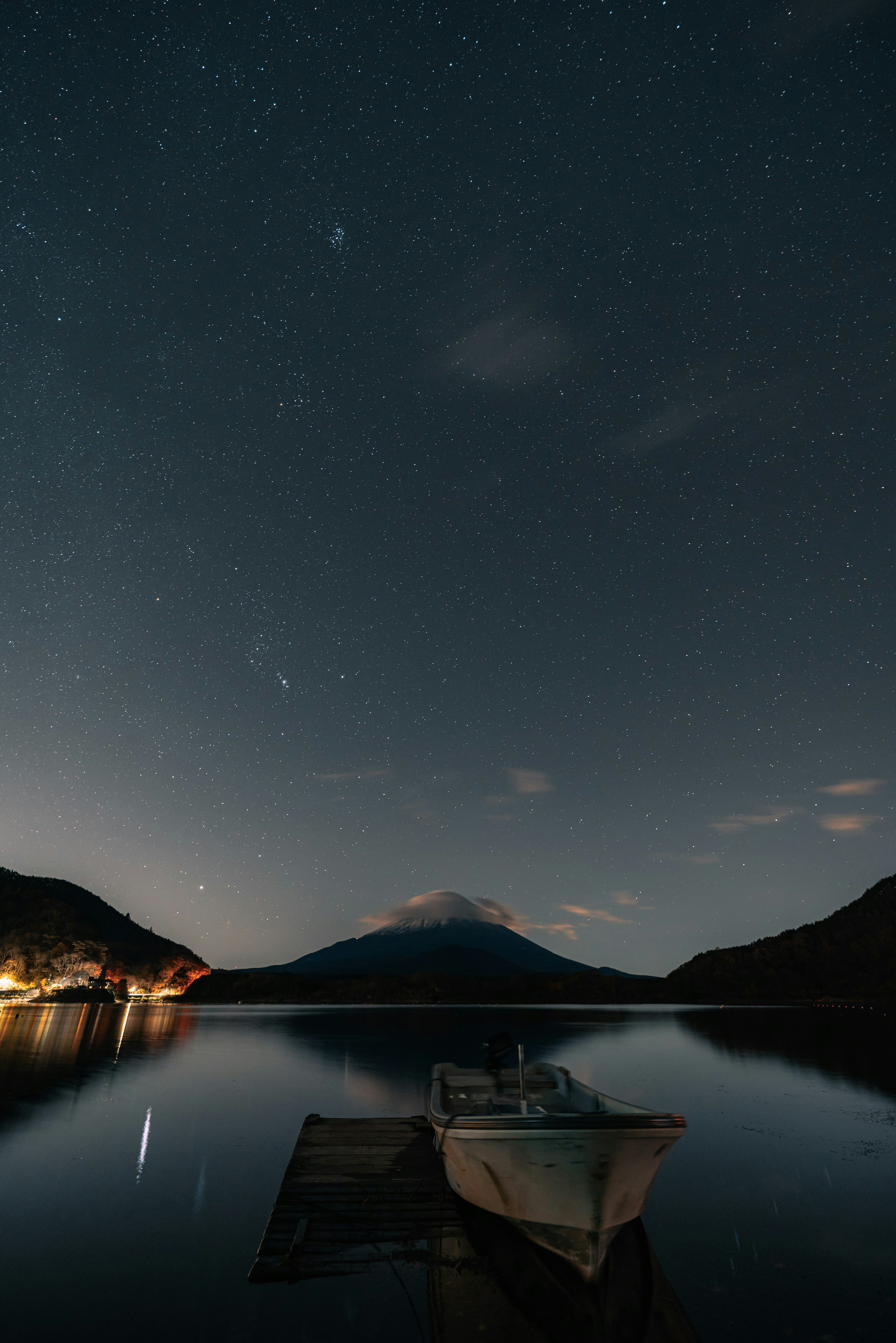 Un pequeño barco en un lago tranquilo bajo un cielo estrellado con montañas de fondo