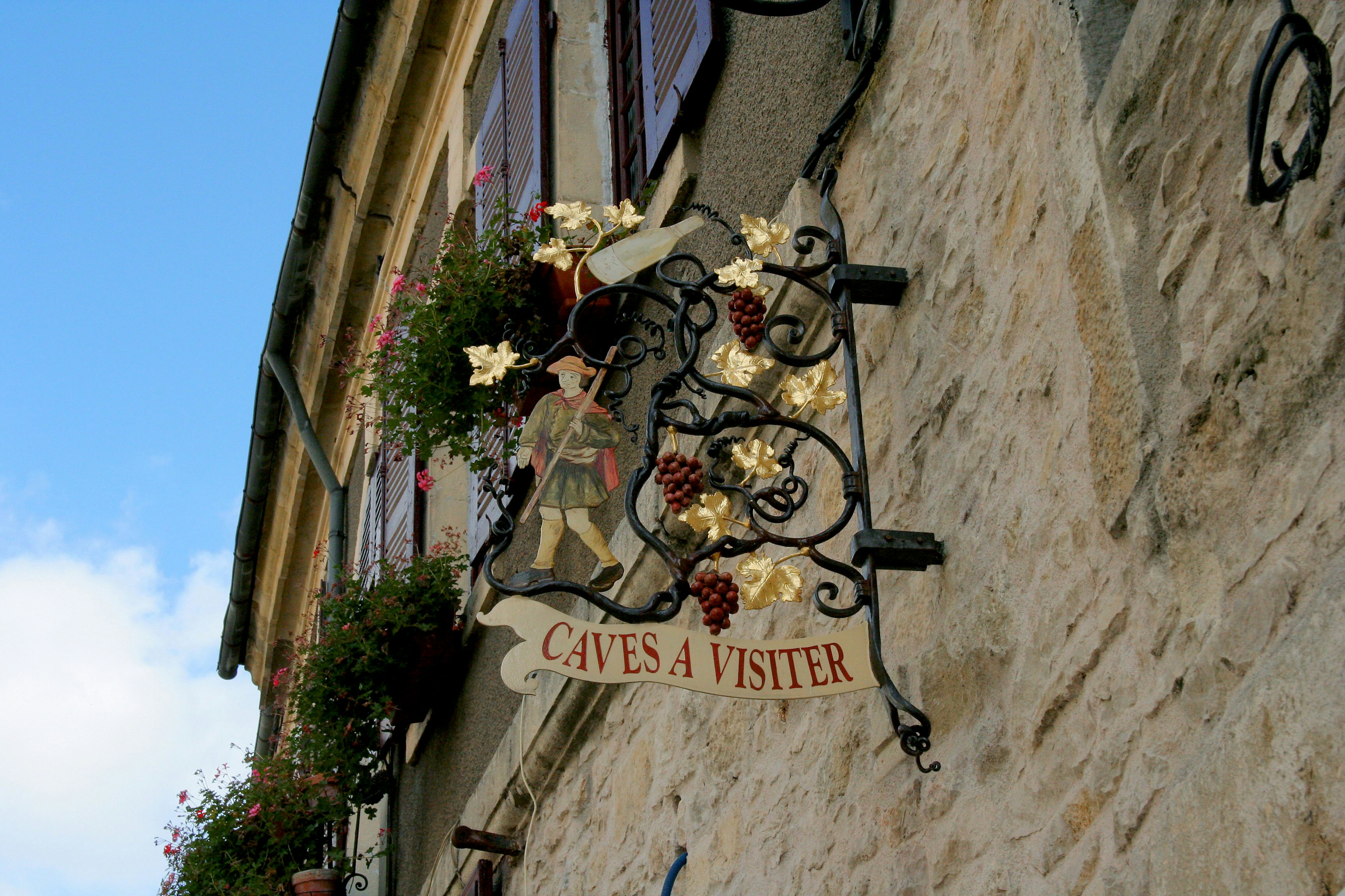 Schönes Schild, das an einer Steinmauer hängt, mit floralen und Traubendekorationen für ein französisches Weingeschäft