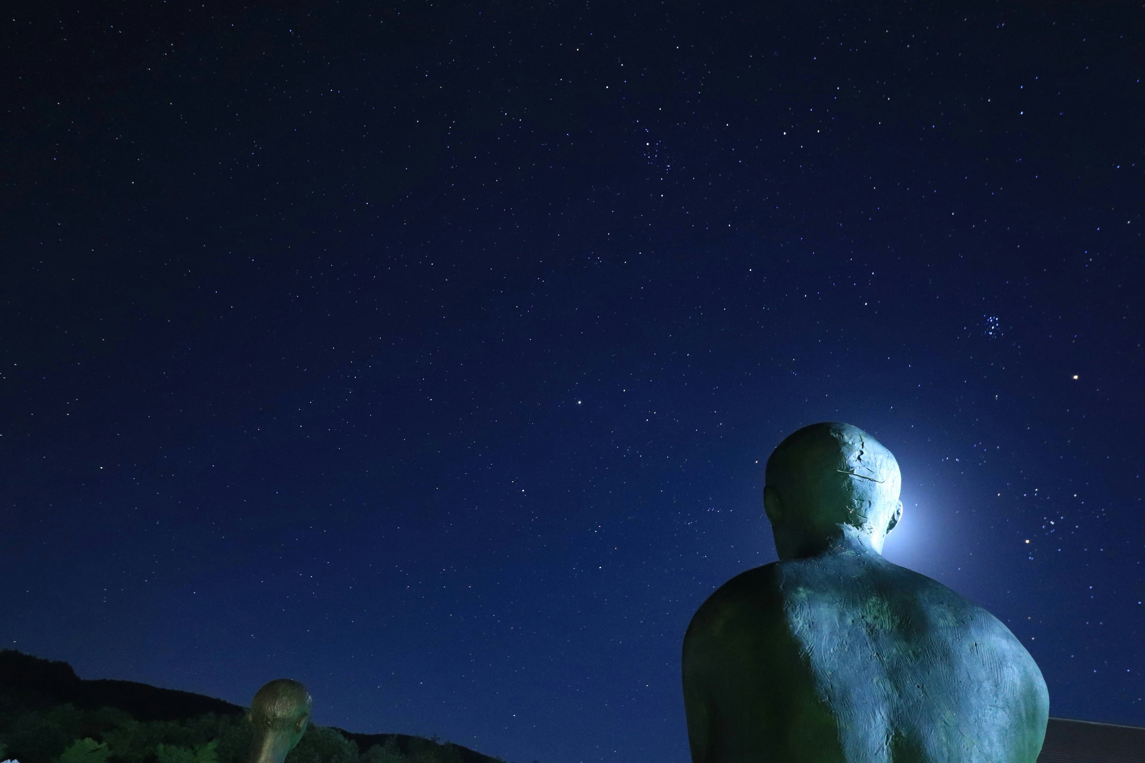 Escultura mirando al cielo estrellado con luna llena