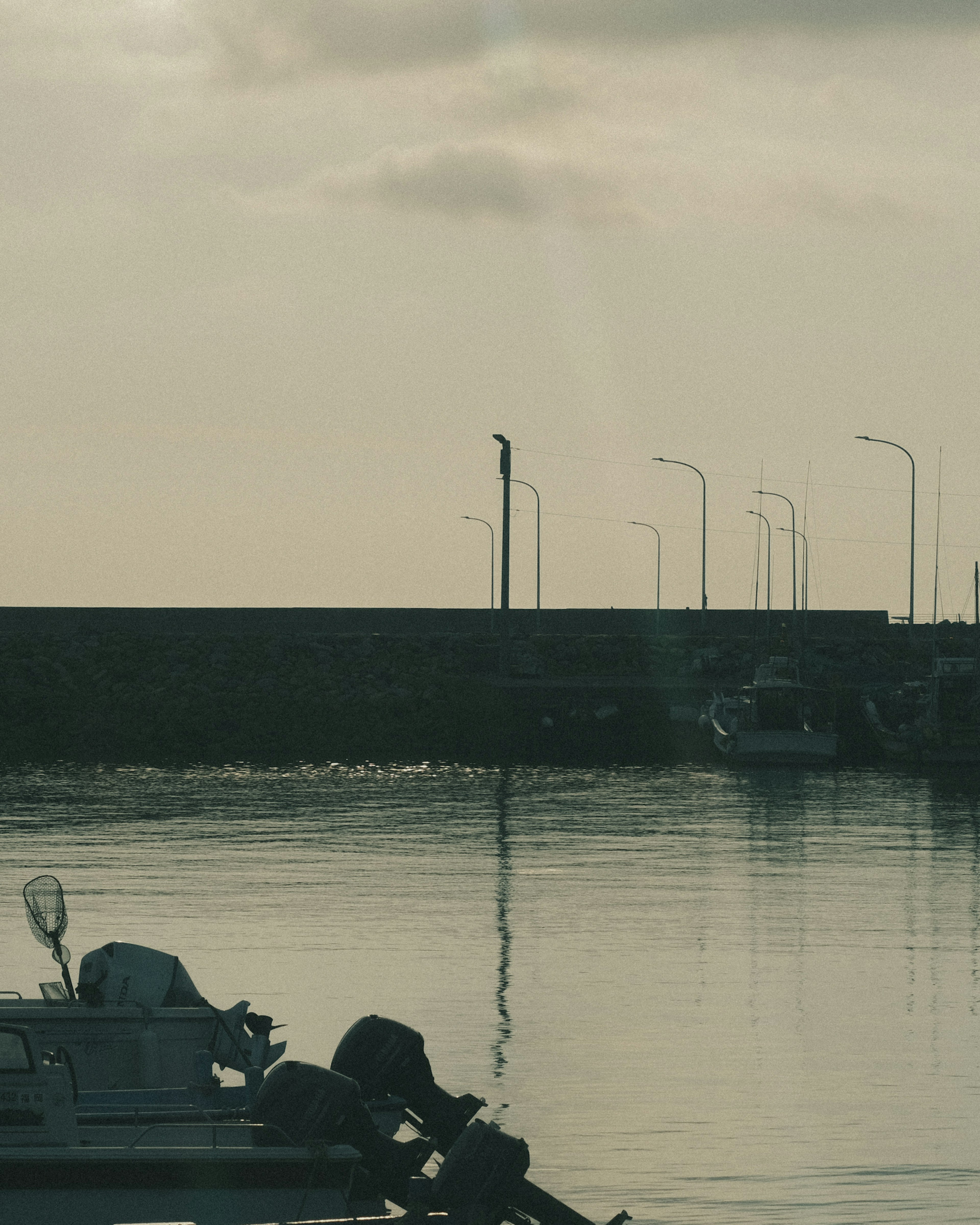 Escena de puerto tranquilo con botes y agua calma que presenta un faro y un rompeolas