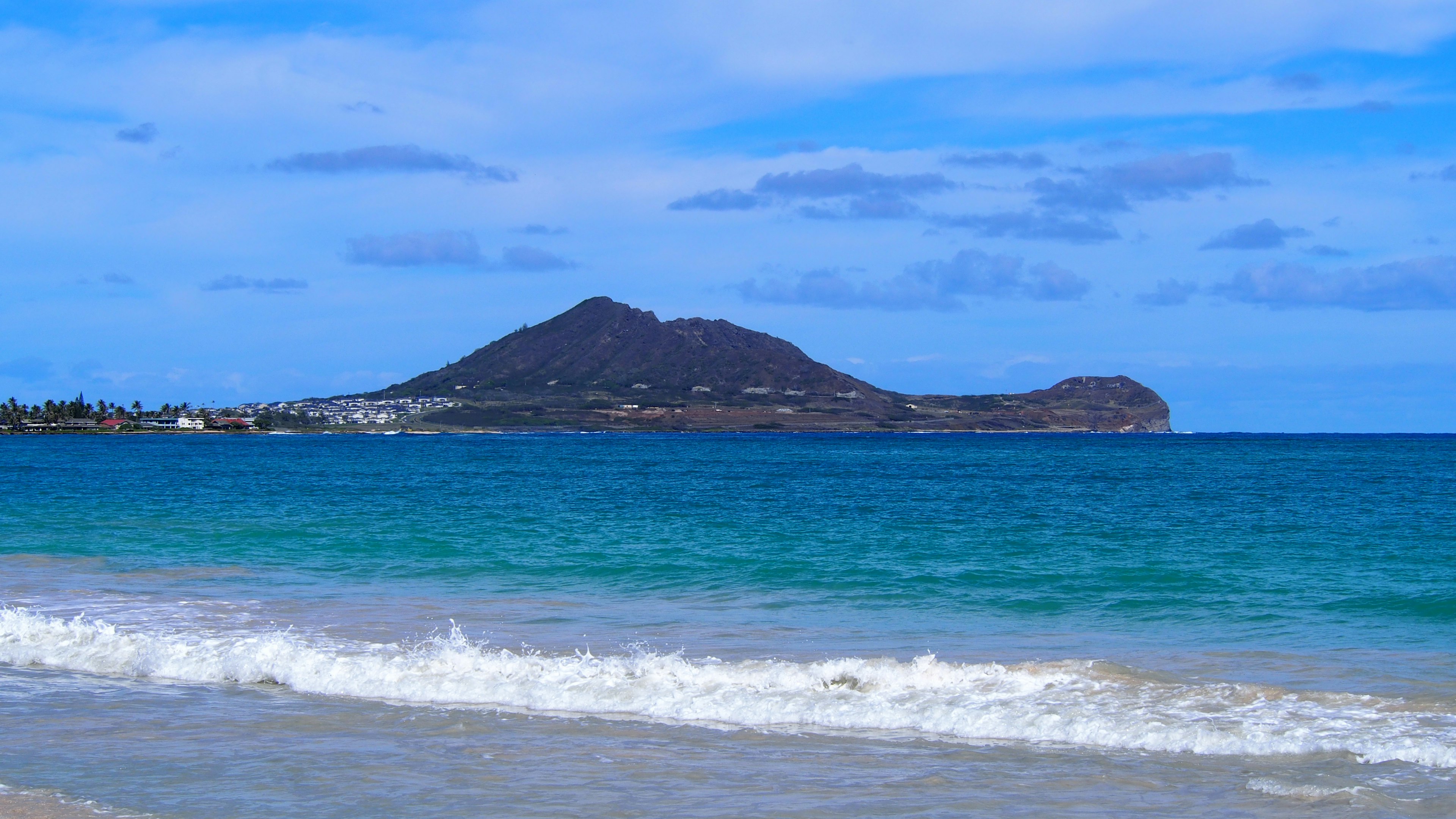 Vista panoramica di una spiaggia con onde calme e oceano blu con una montagna sullo sfondo