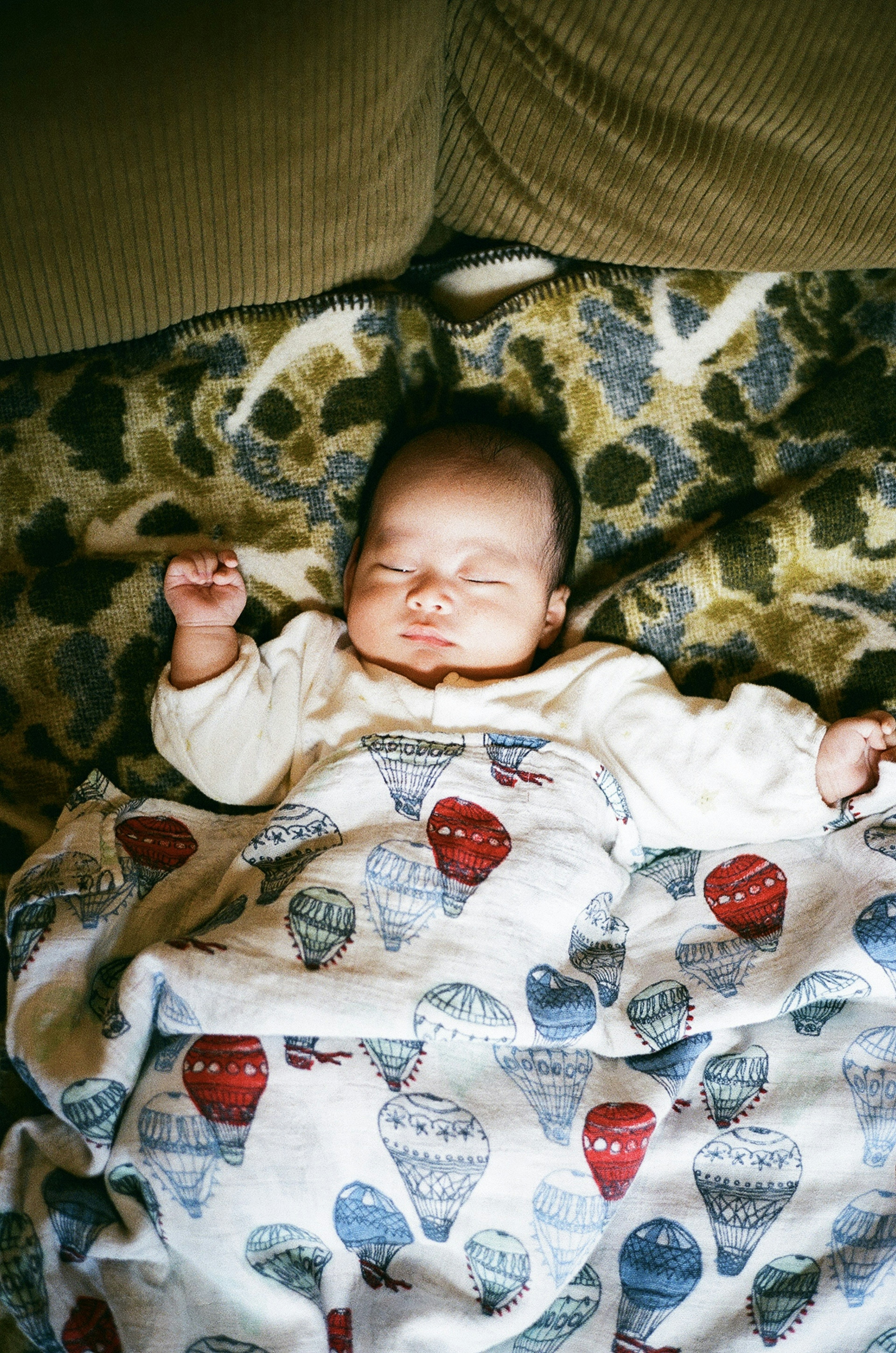 A baby peacefully sleeping wrapped in a blanket with hot air balloon patterns