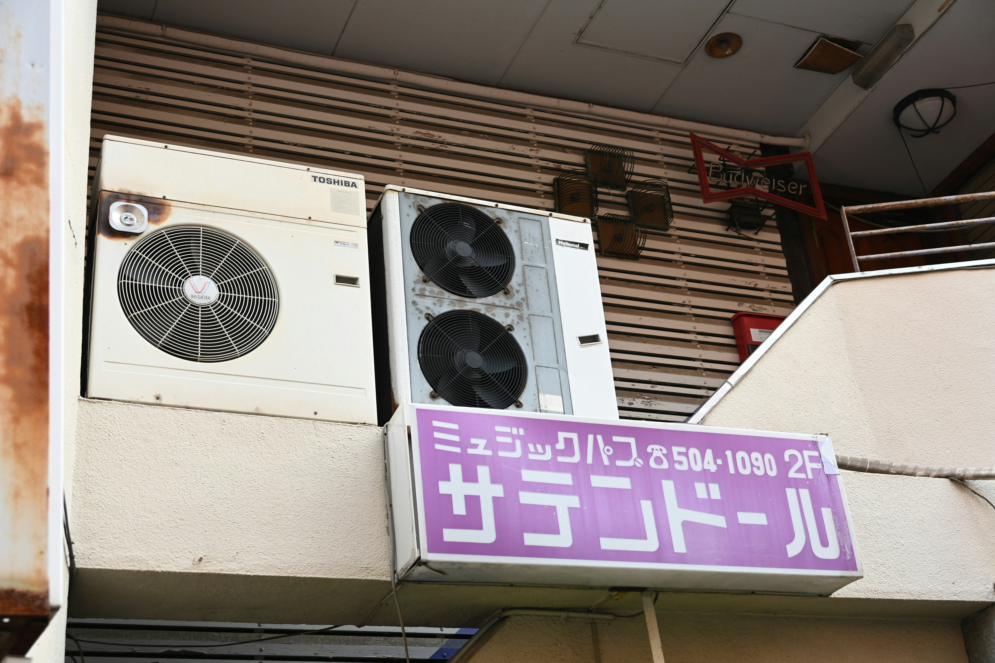 Exterior view of a building with air conditioning units and a purple sign