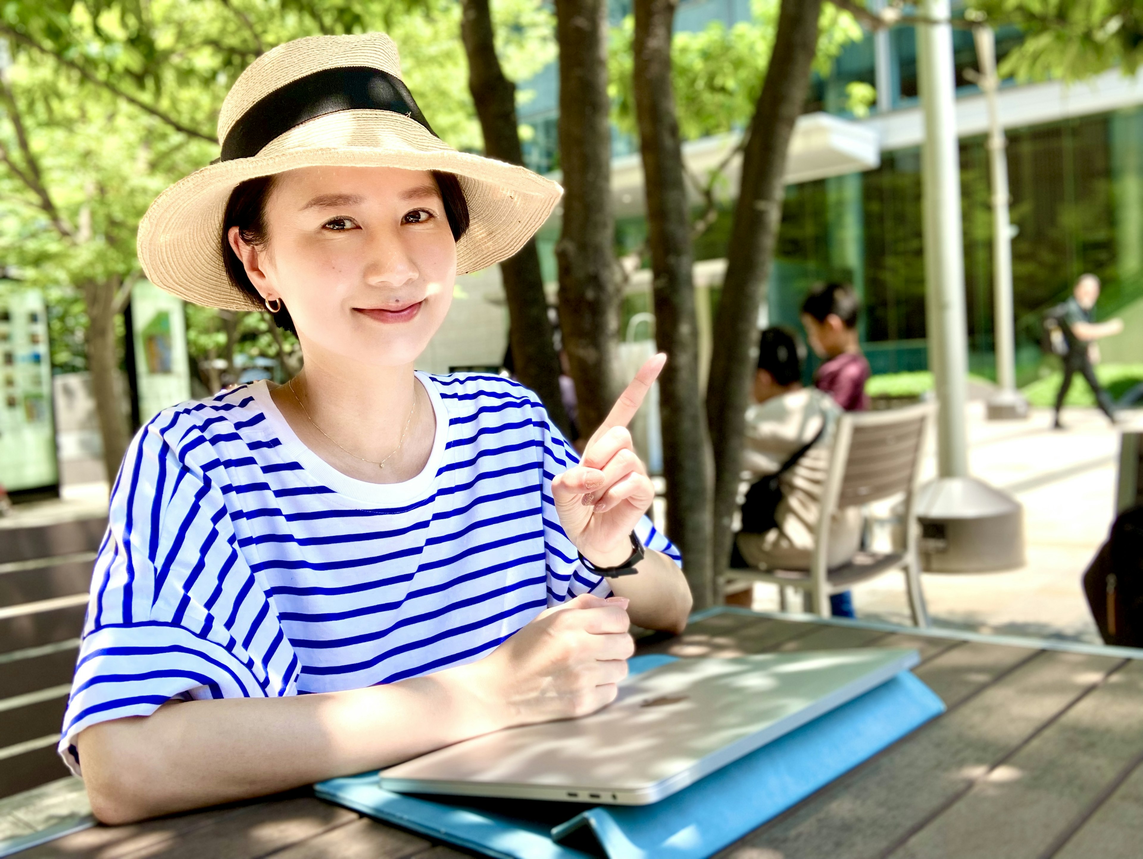 Smiling woman in a striped shirt pointing while sitting outdoors