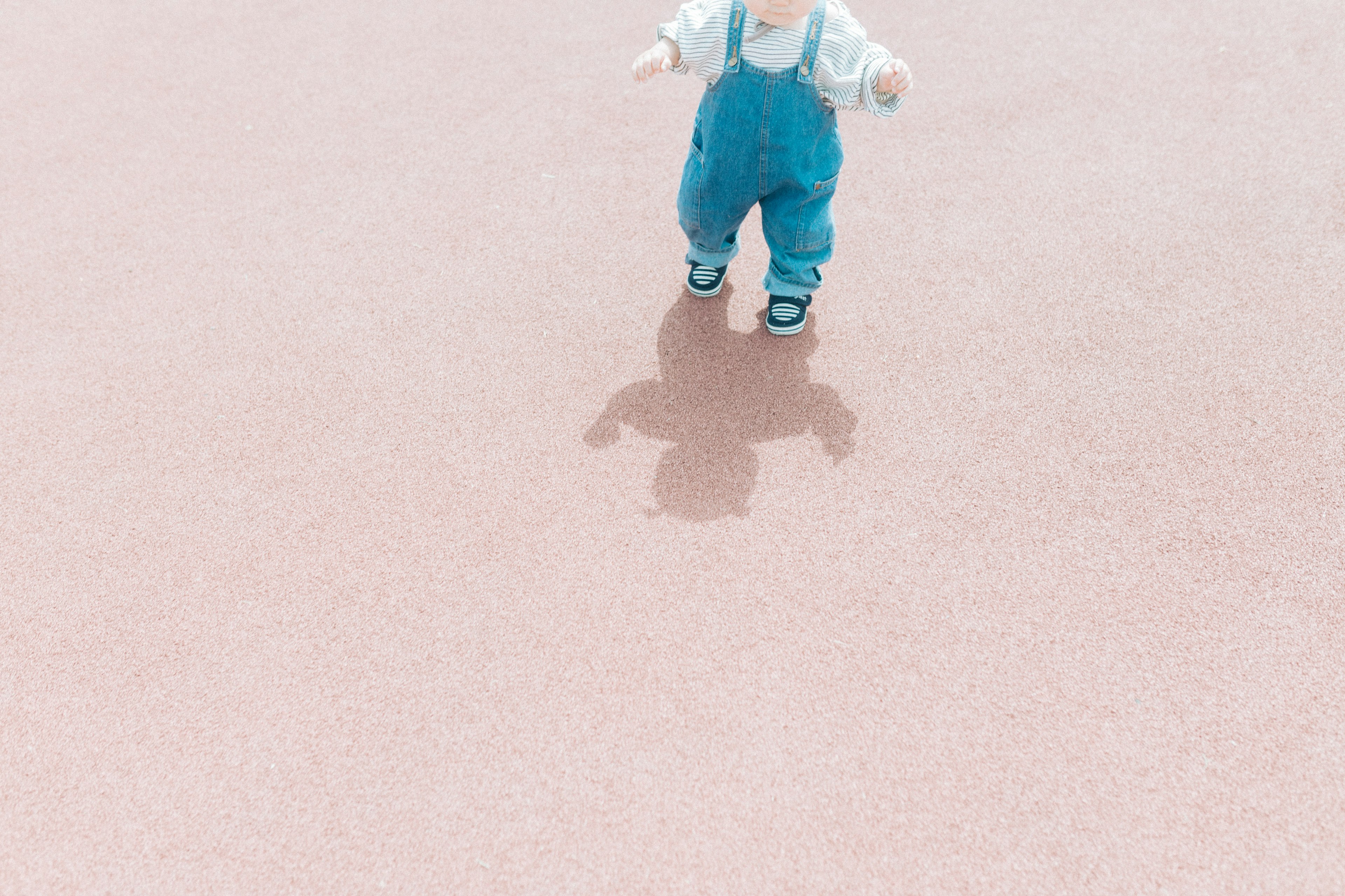 Baby wearing blue overalls standing on a pink surface