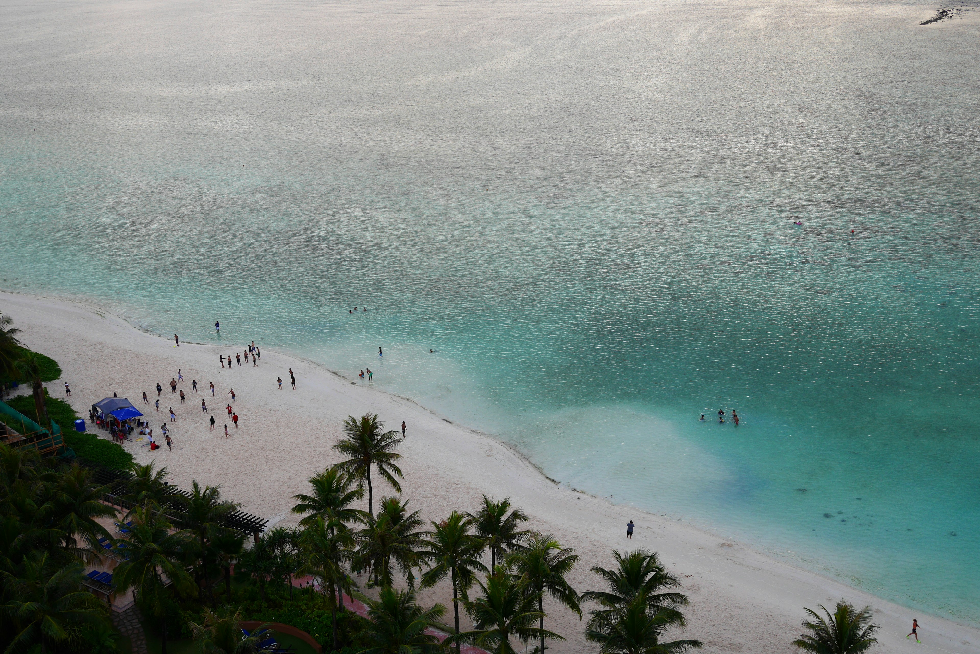 Pemandangan pantai dengan lautan biru dan pasir putih orang-orang menikmati air