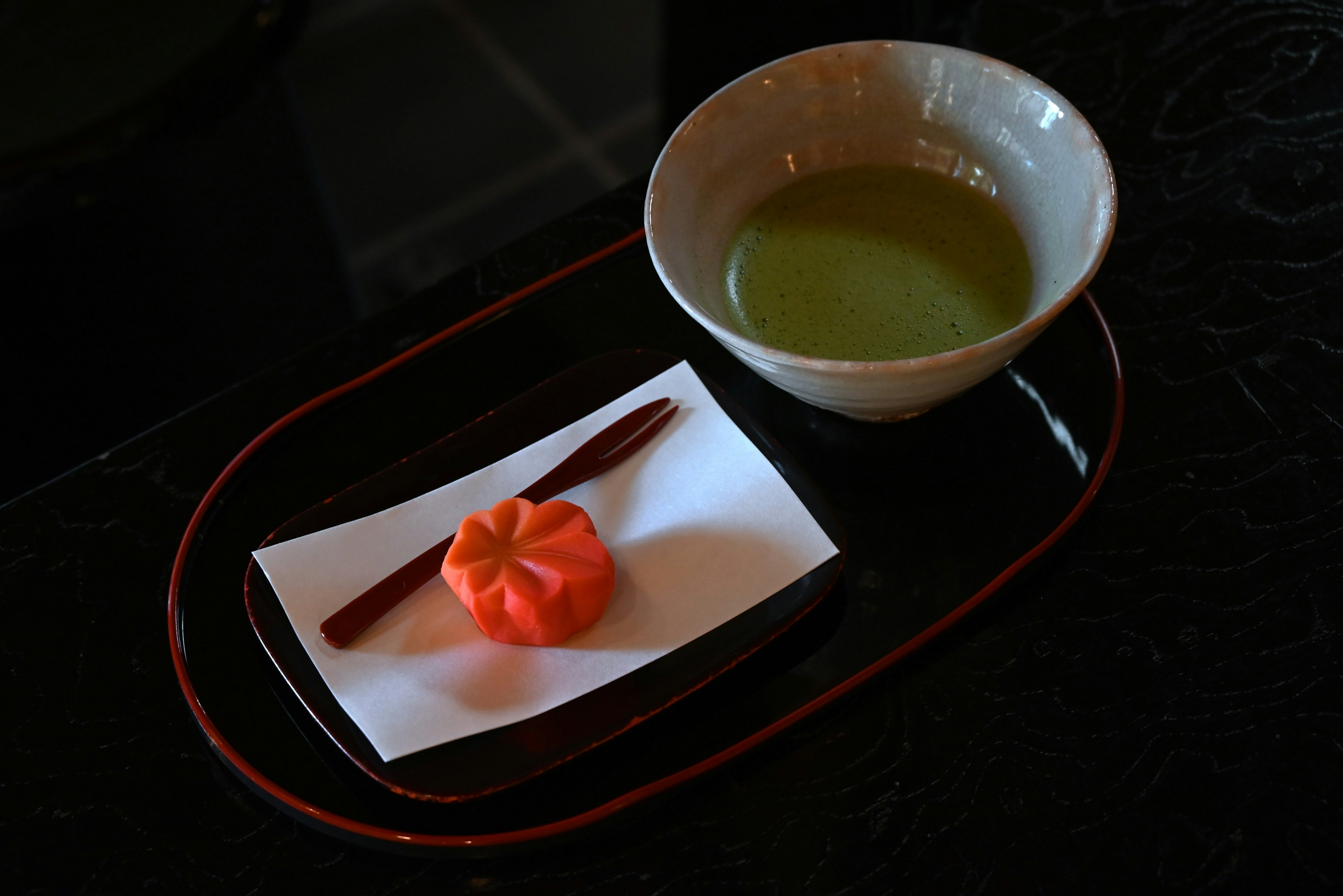 Un tazón de té verde junto a un dulce japonés rojo sobre papel blanco