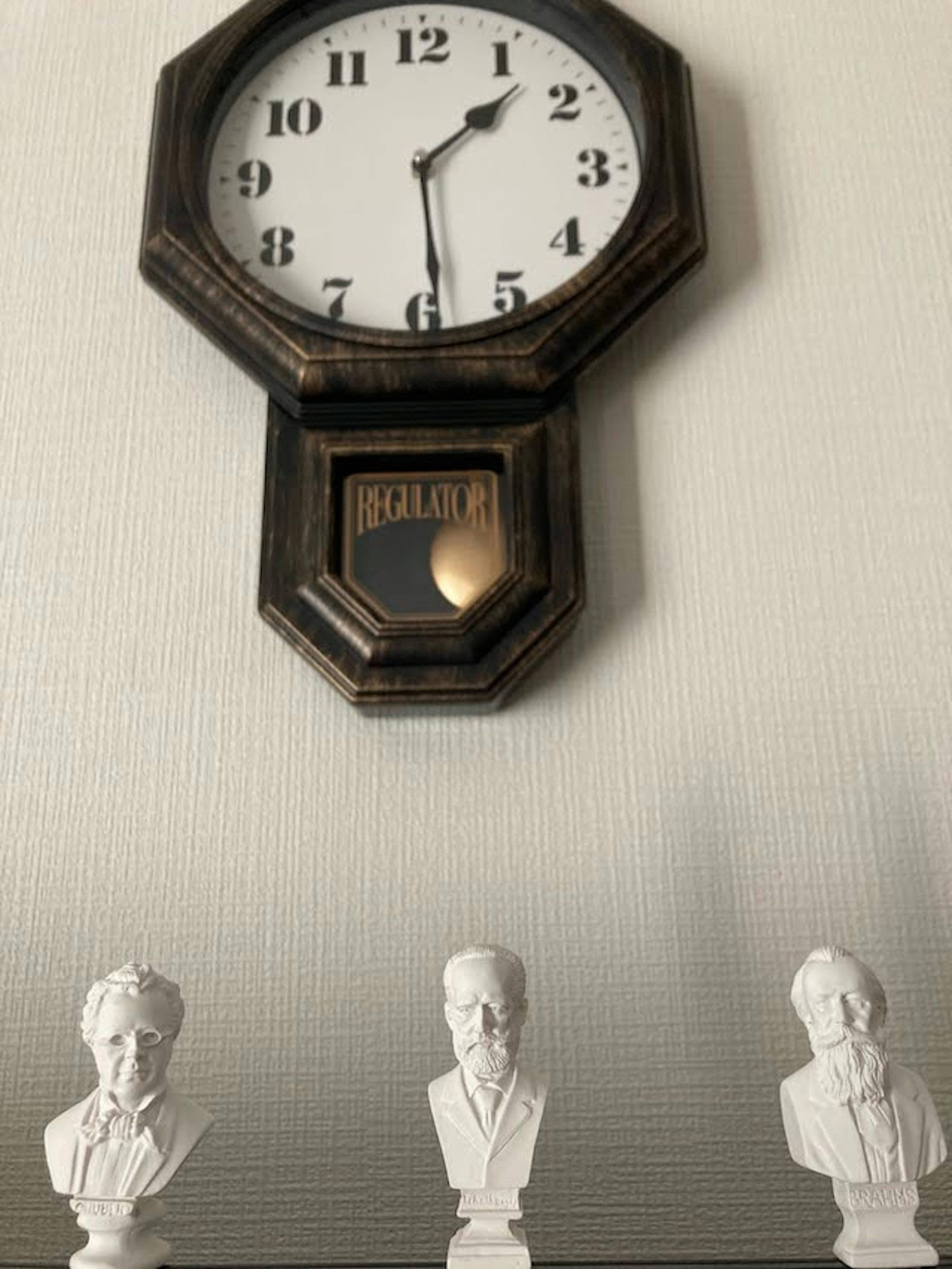 Octagonal wall clock with white bust sculptures underneath