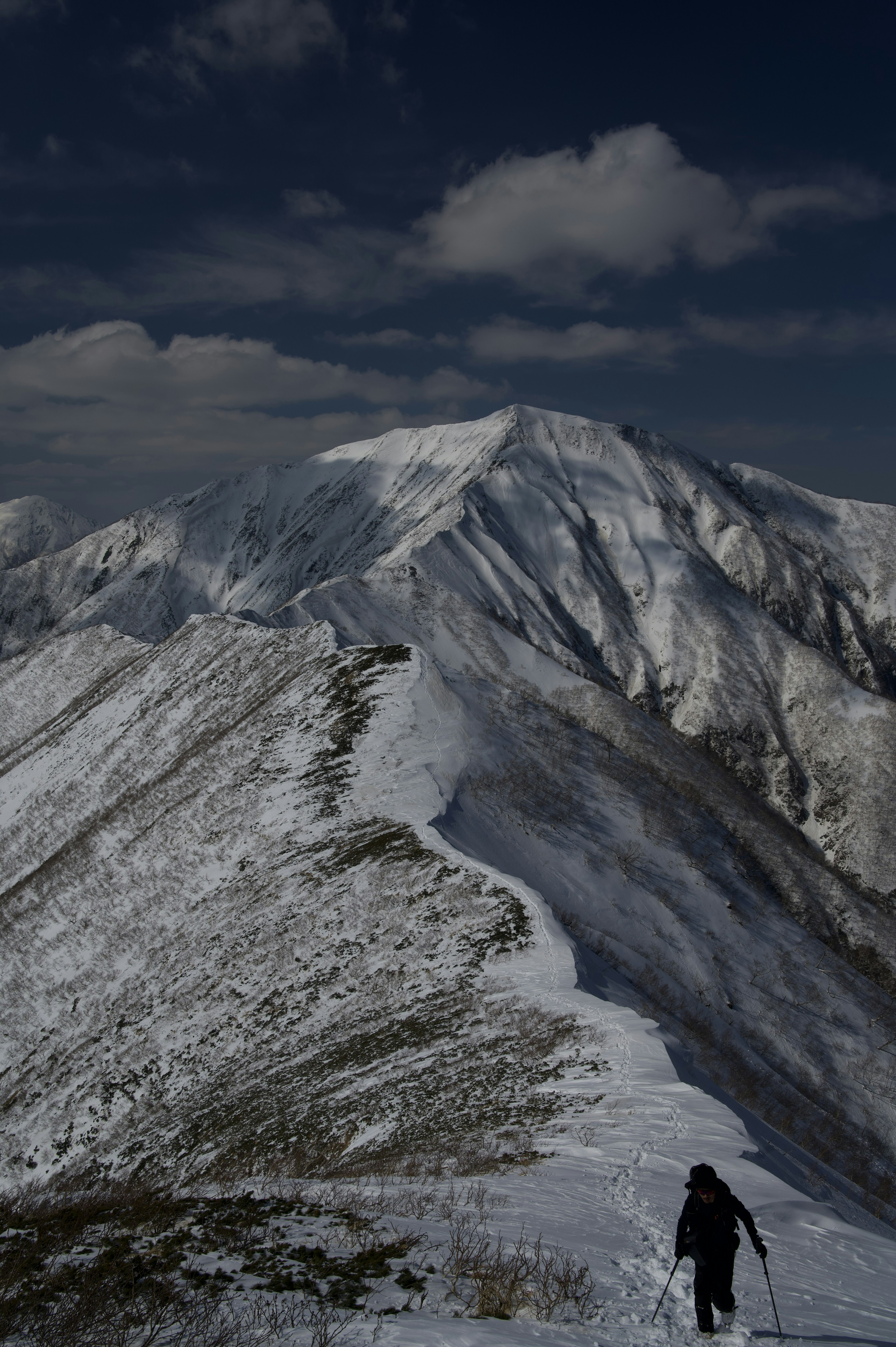 Wanderer, der auf einem verschneiten Gebirgskamm mit dramatischen Gipfeln im Hintergrund geht