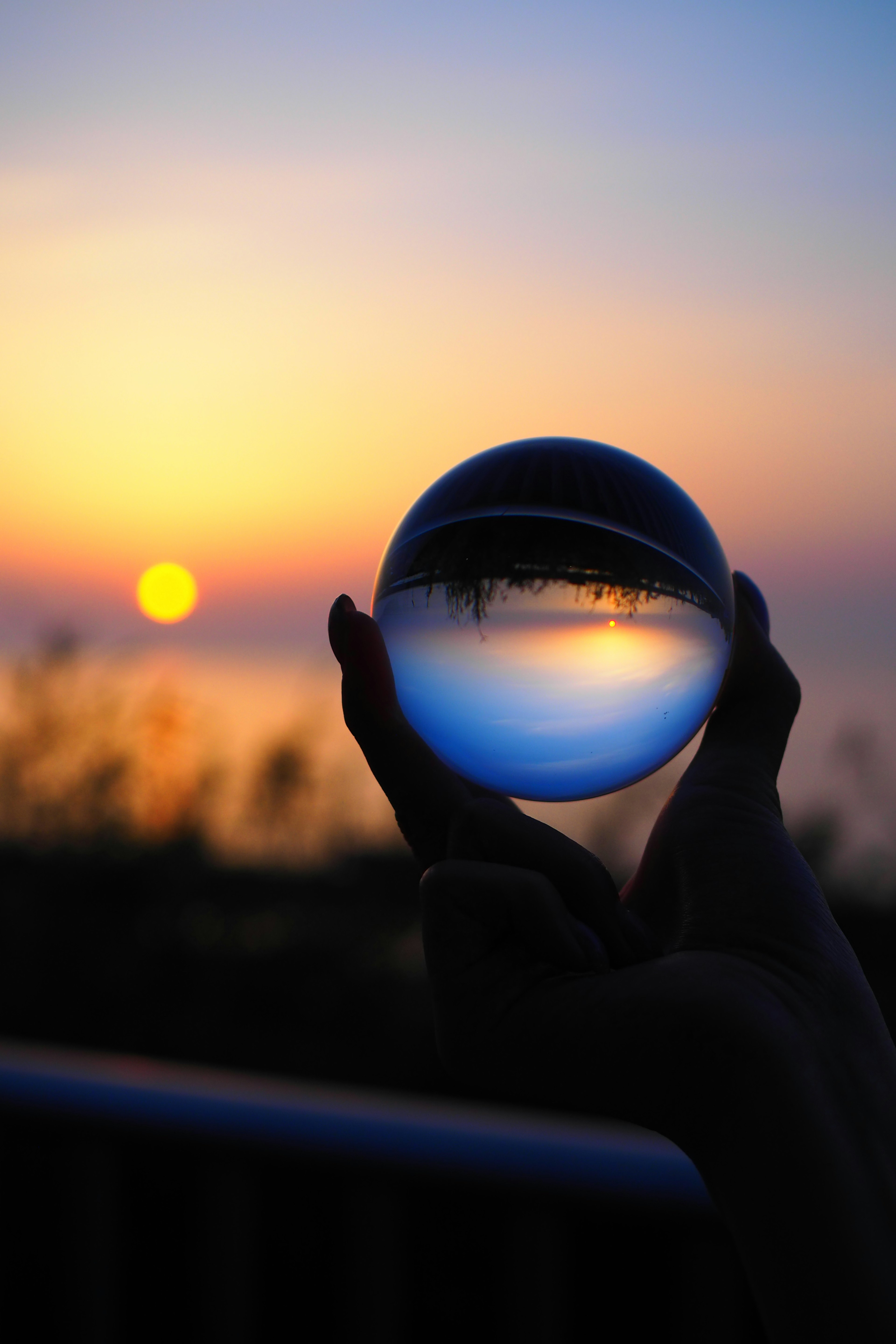 Silhouette einer Hand, die eine Glaskugel gegen einen Sonnenuntergang hält