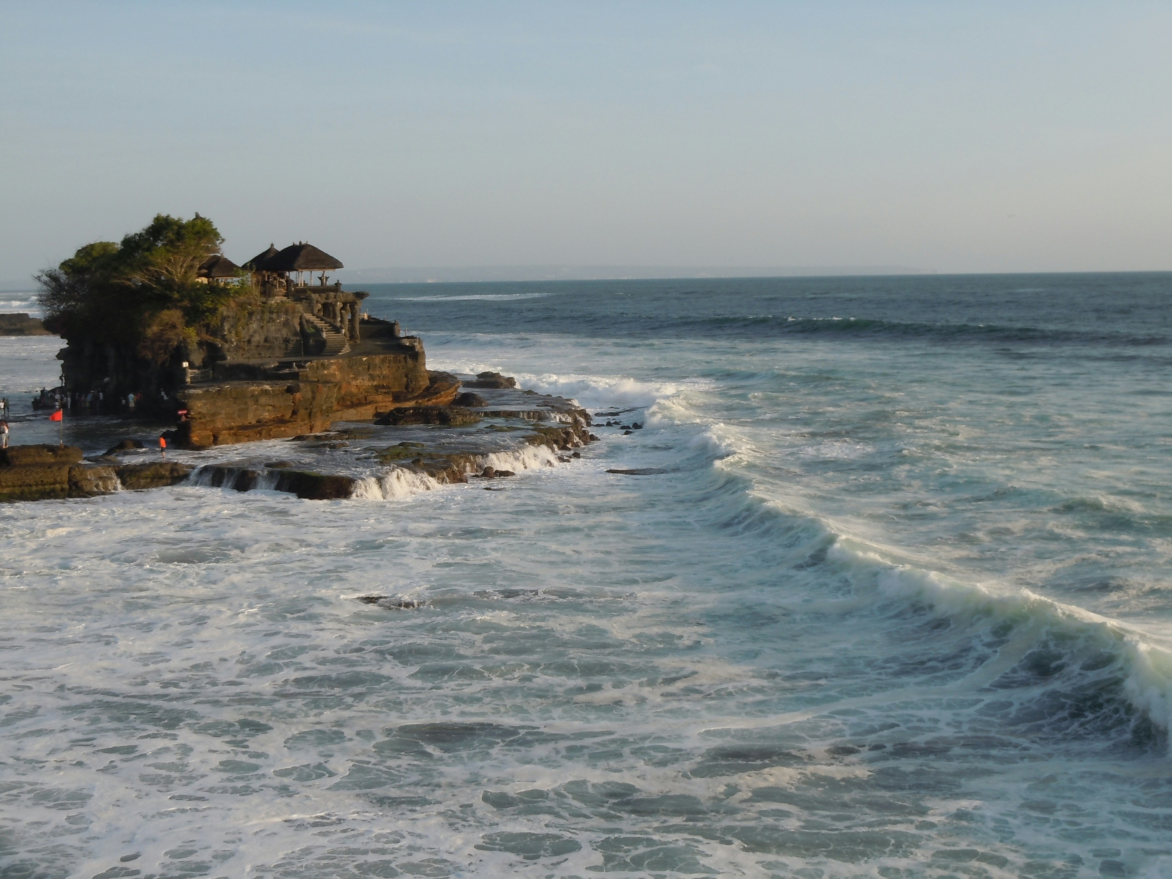 Small rocky island with a hut on the coast where waves crash