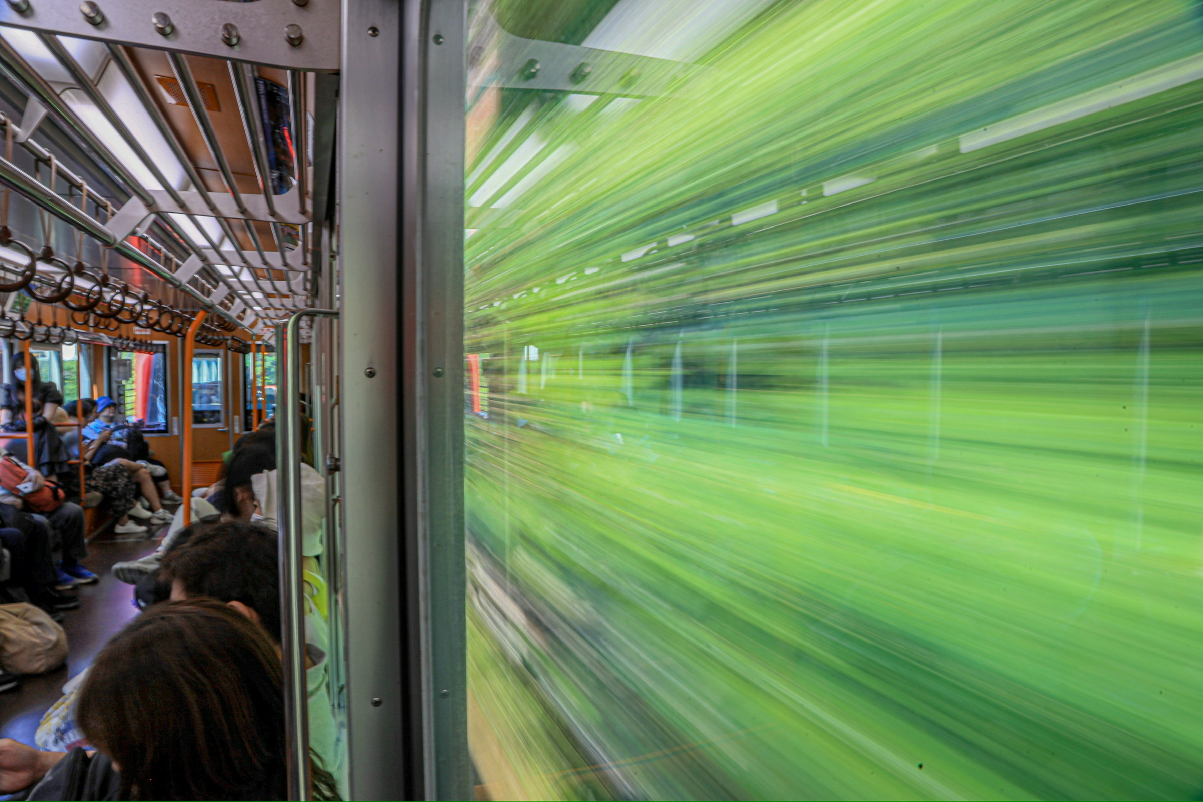 View of blurred green landscape from inside a train with passengers