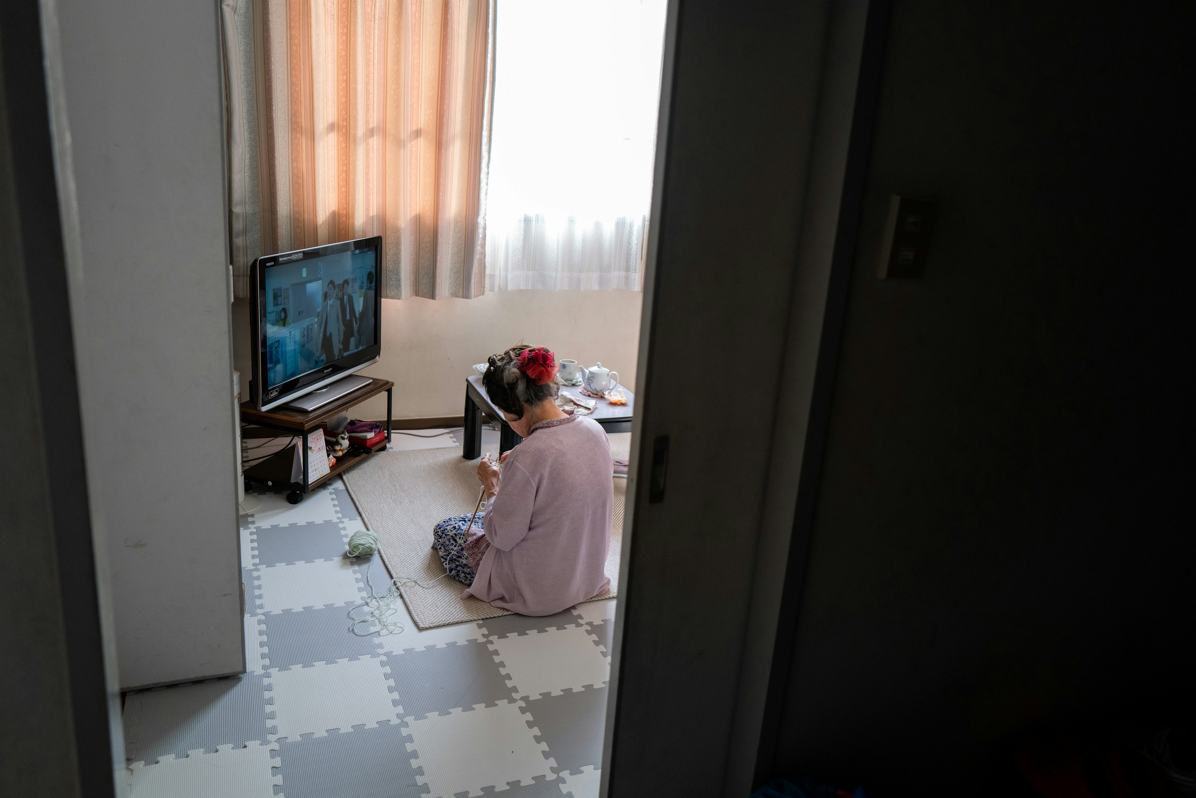 Eine Person, die auf dem Boden sitzt und in einem hellen Raum nahe einem Fenster fern sieht