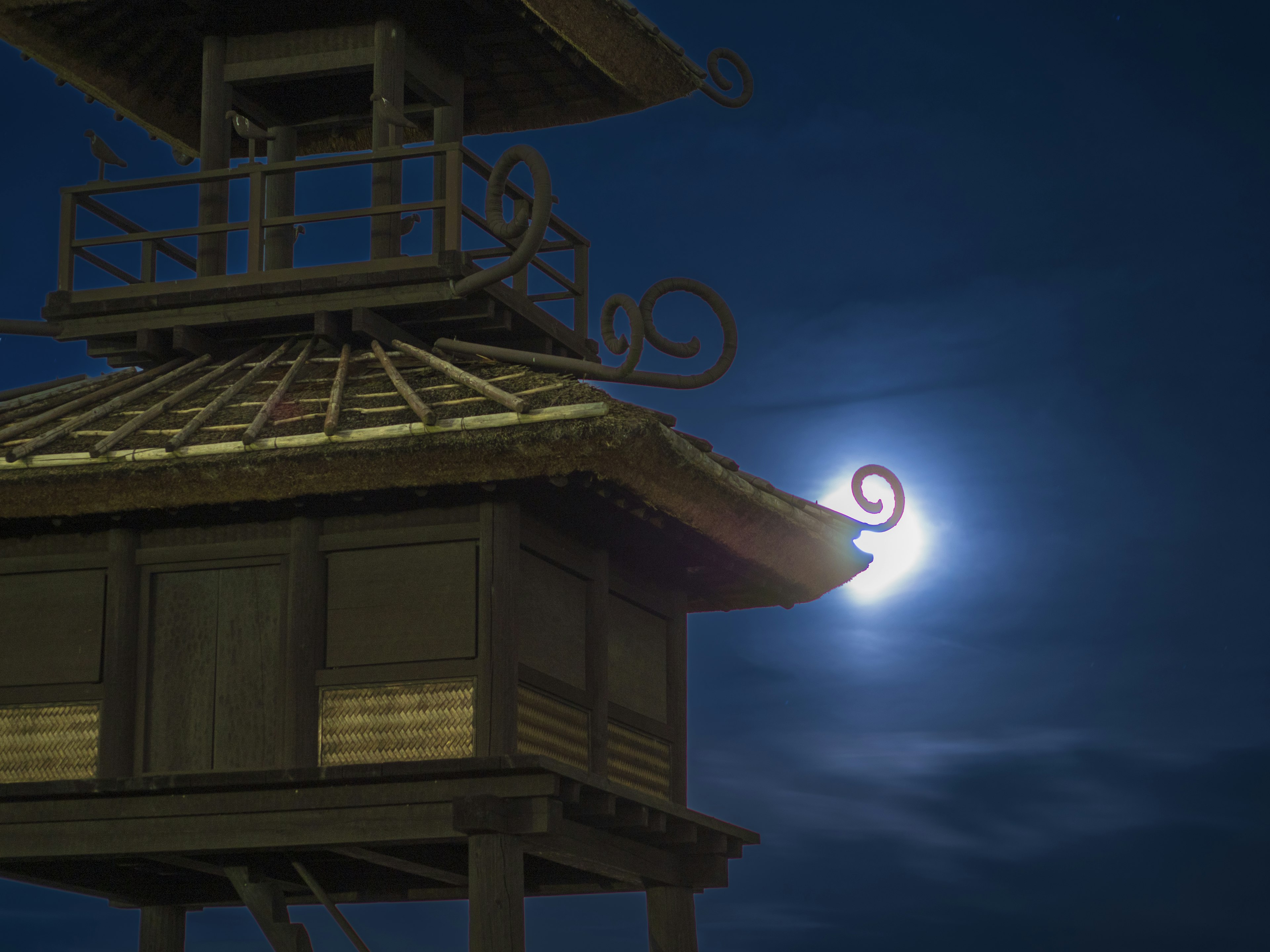 Toit d'un bâtiment traditionnel sous une lune brillante dans un ciel nocturne