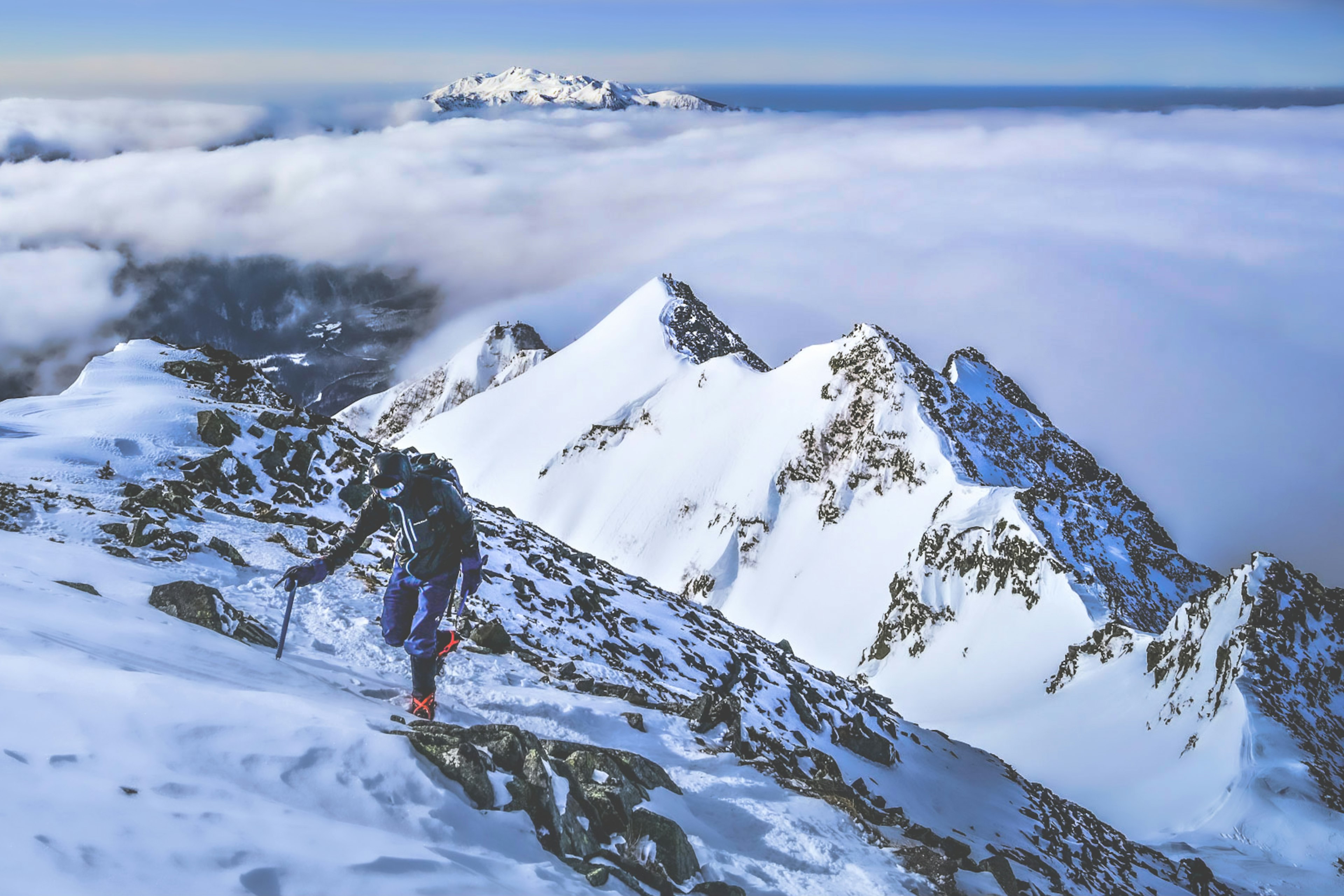 Ein Bergsteiger, der einen schneebedeckten Berg mit einer Wolkenmeer und blauem Himmel erklimmt