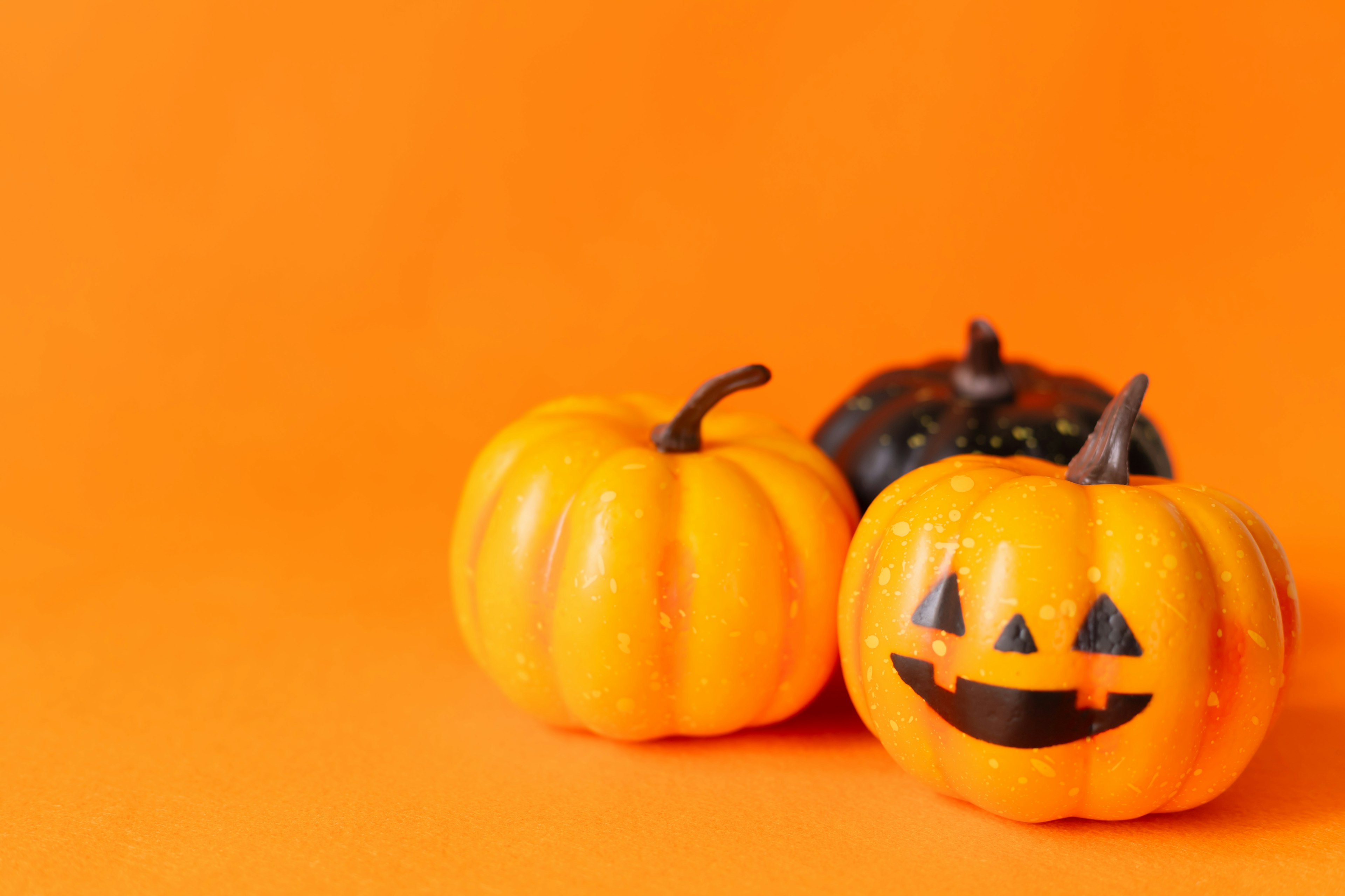 Small pumpkins with a jack-o'-lantern face against an orange background