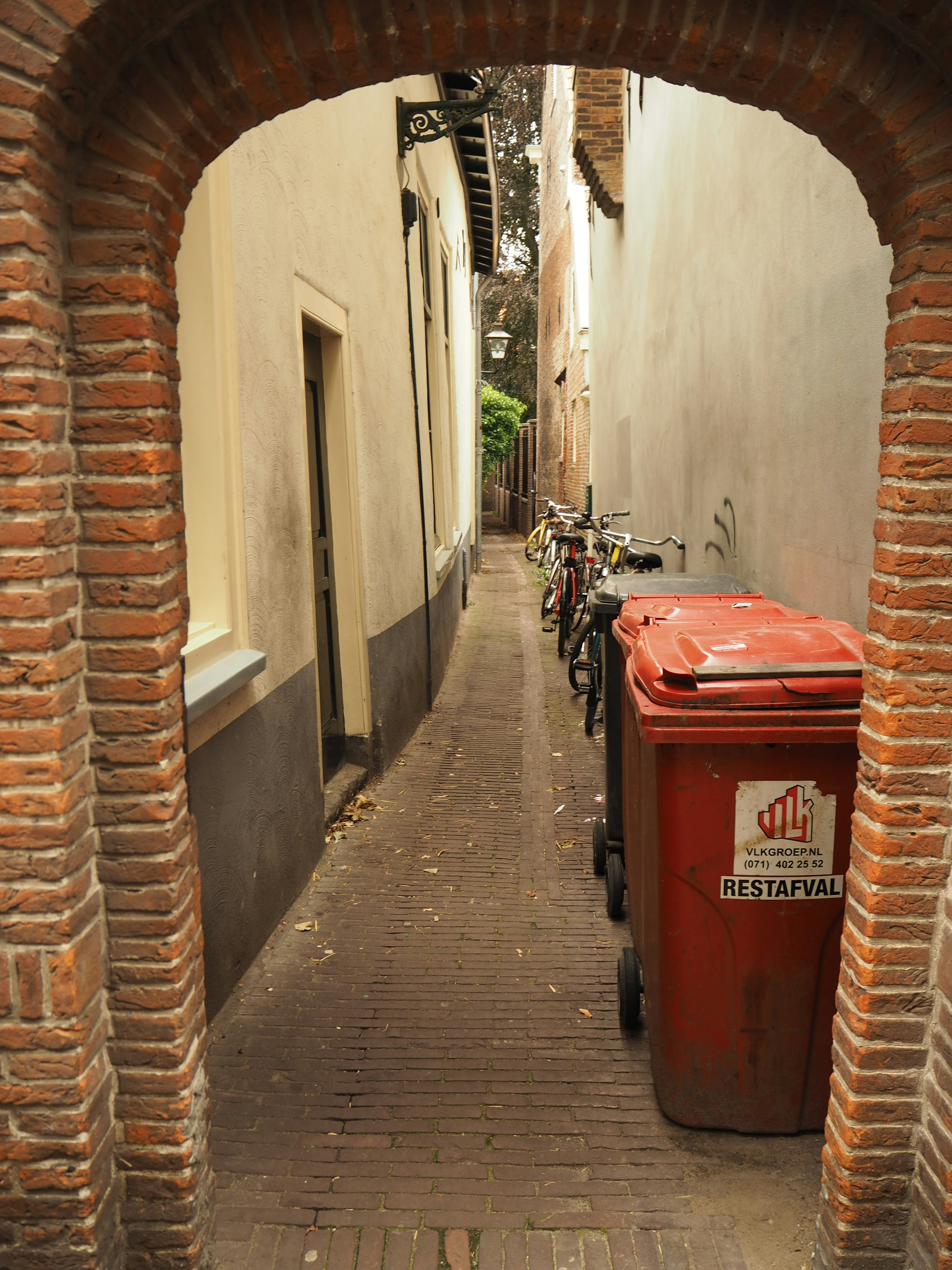 Lorong sempit dengan tempat sampah merah dan sepeda di bawah lengkungan