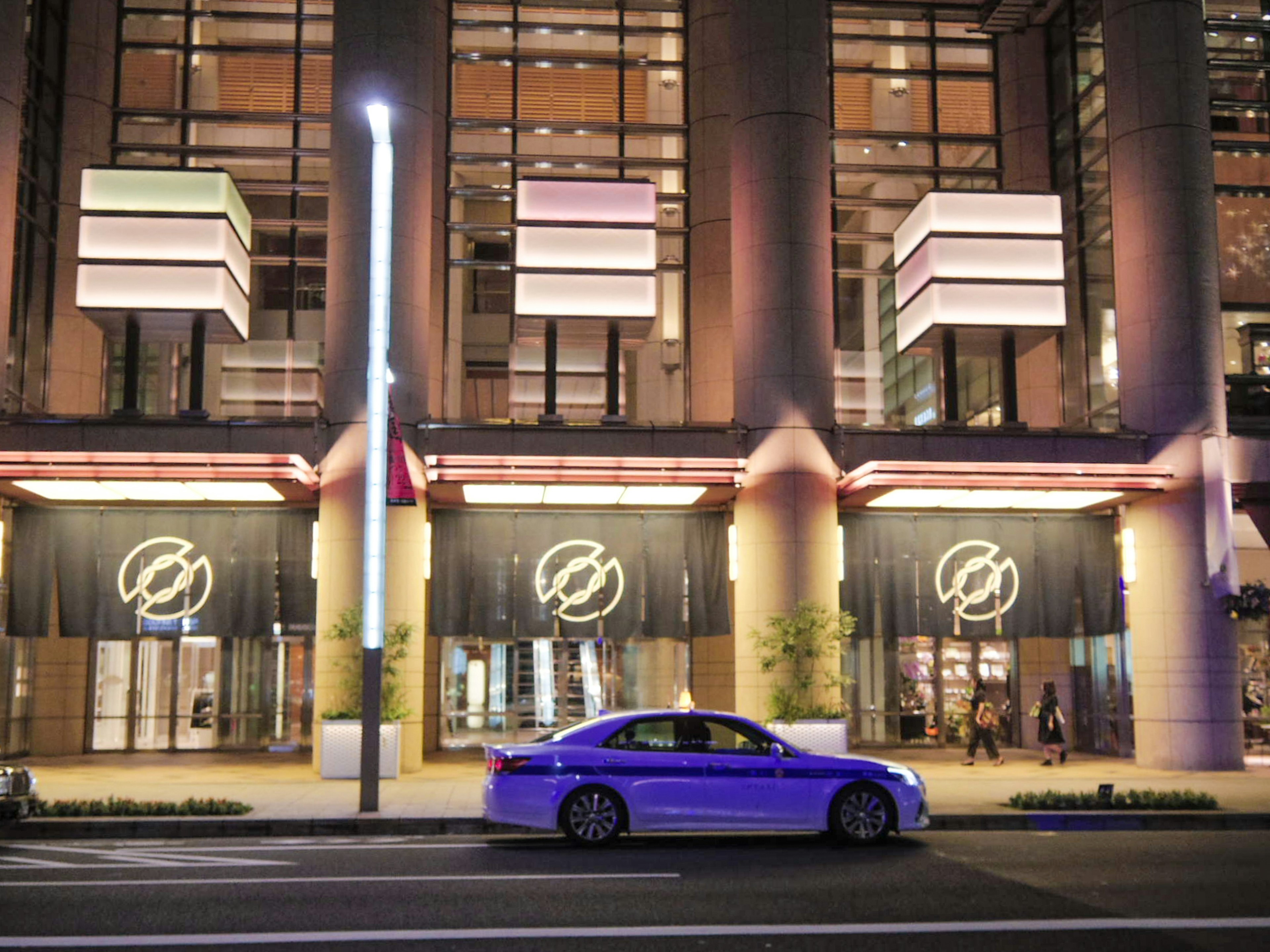 Modern building exterior in cityscape at night with a purple car