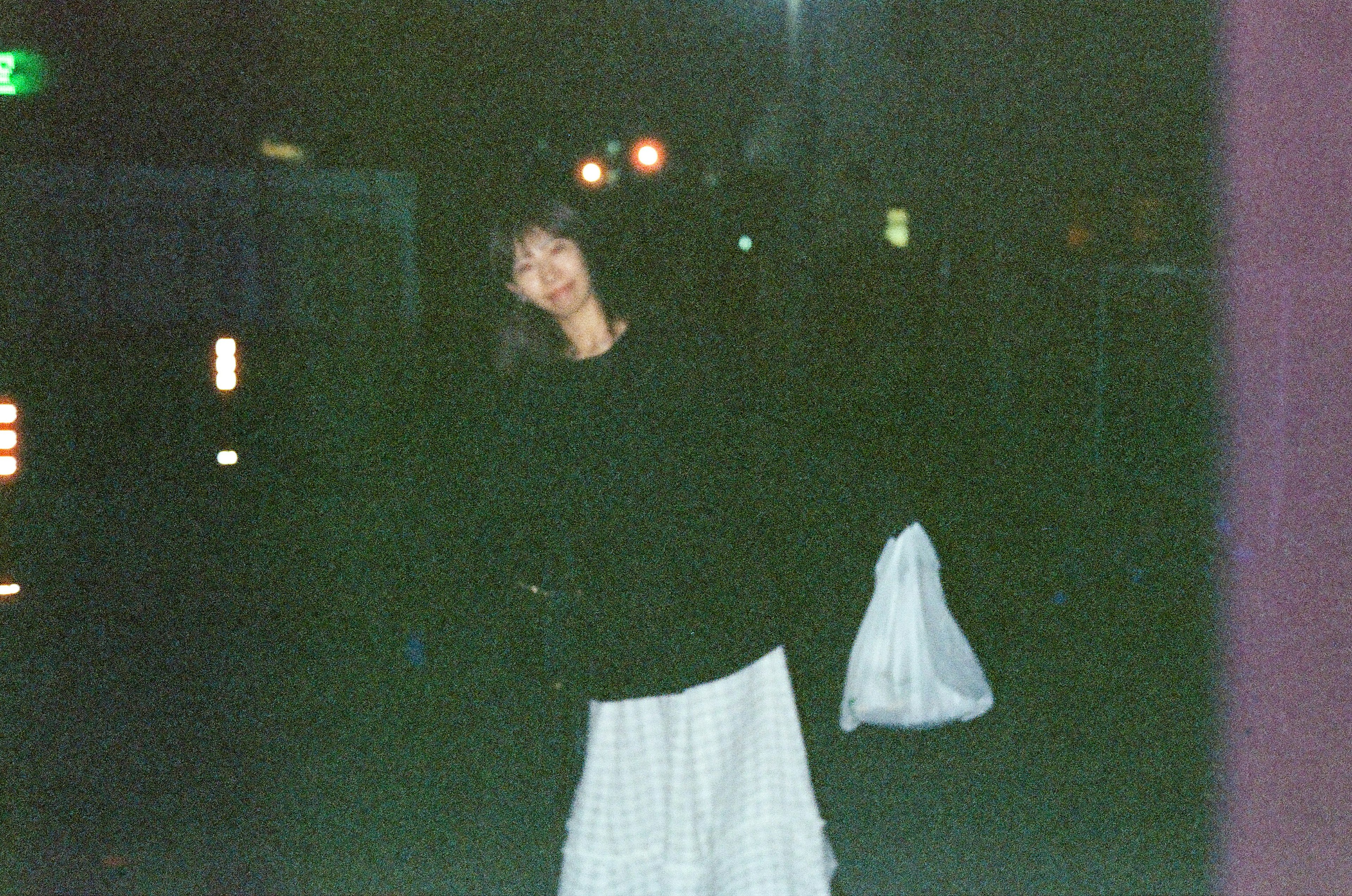 Woman in a black top and white skirt standing against a dark background