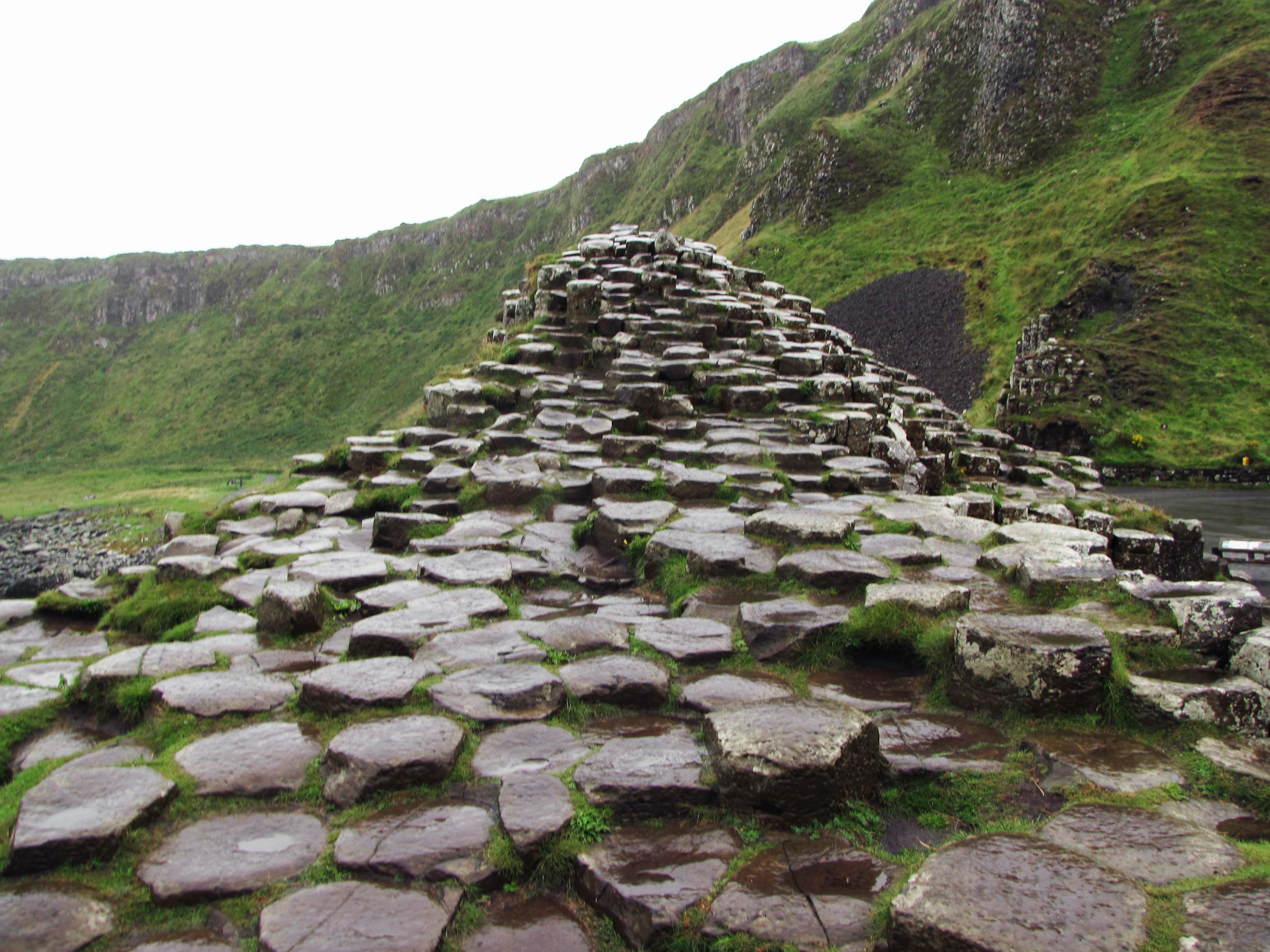 รูปแบบหินหกเหลี่ยมที่ Giant's Causeway ในไอร์แลนด์พร้อมเนินเขาสีเขียวชอุ่ม