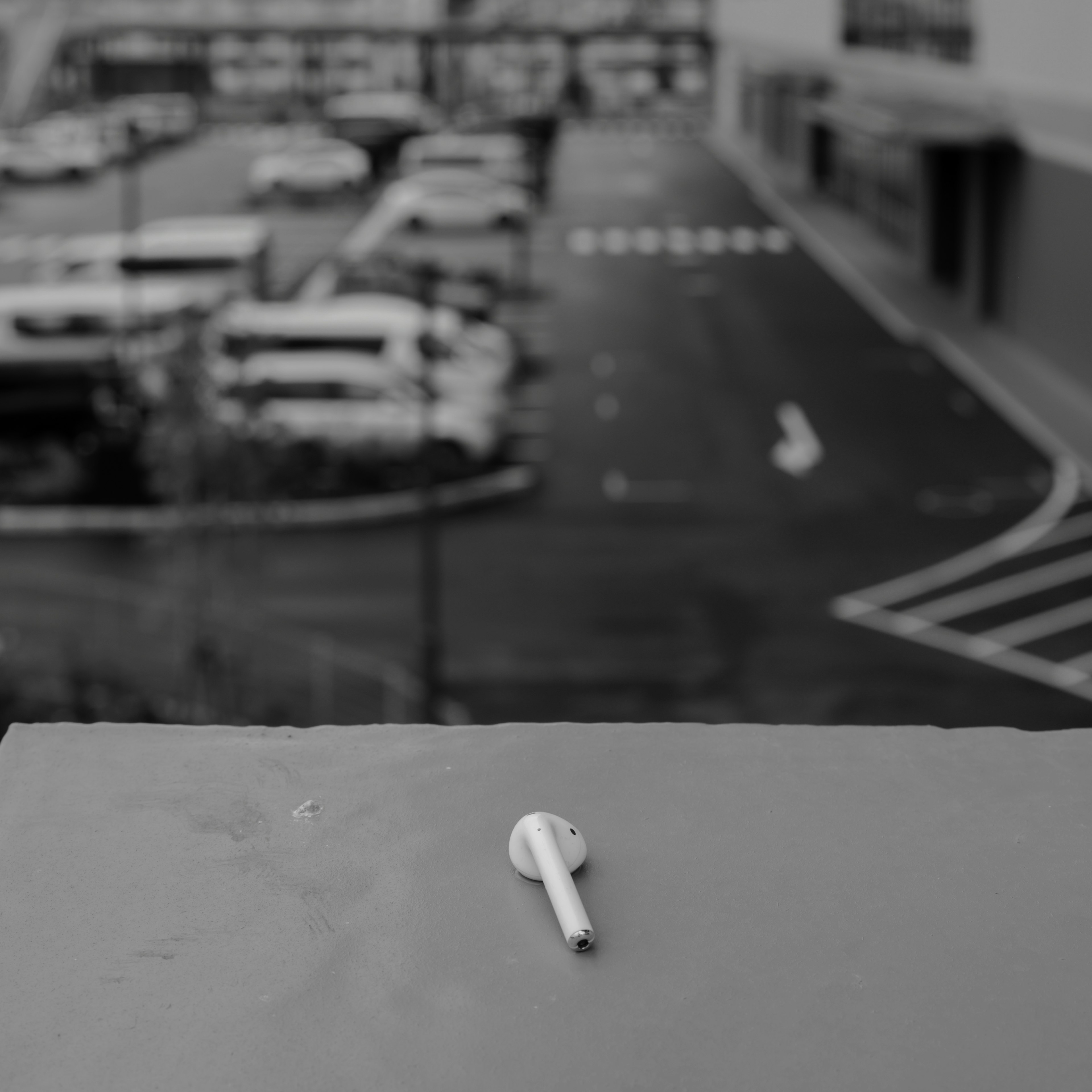 Image en noir et blanc mettant en avant une clé blanche au premier plan avec des voitures floues dans un parking en arrière-plan