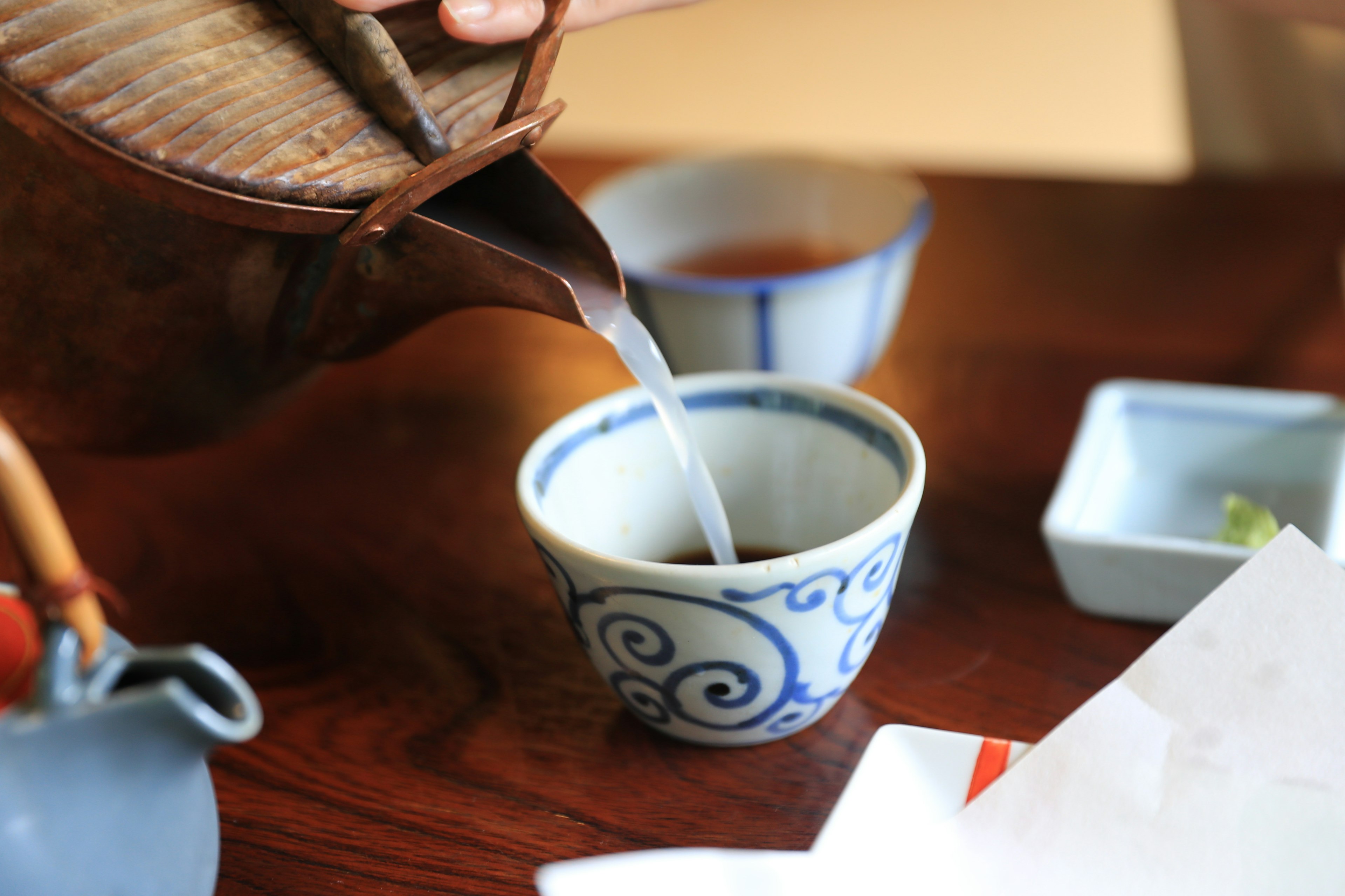 Hand pouring tea into a blue patterned teacup