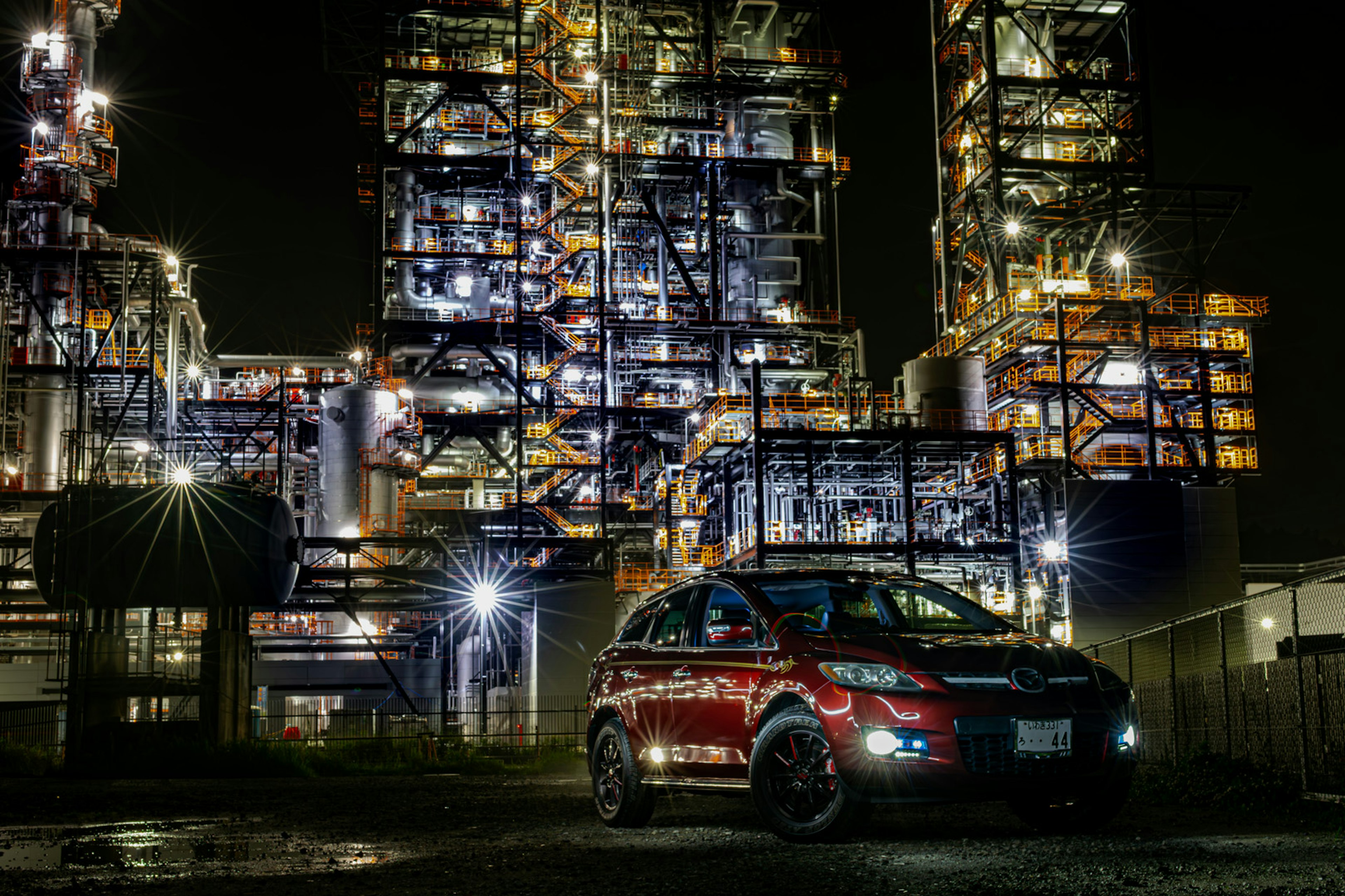 Red SUV parked in front of industrial buildings at night