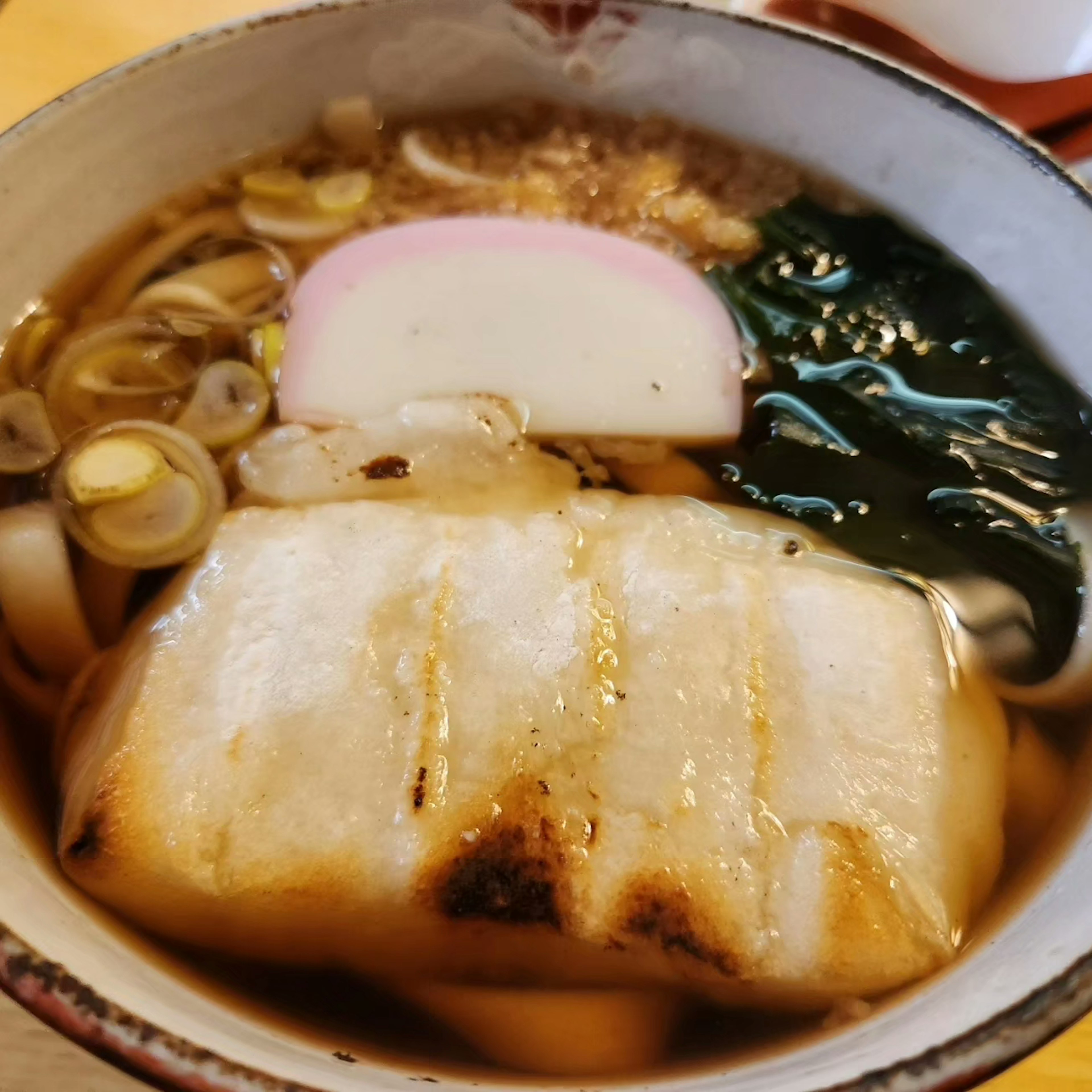 焼き魚のスープに入ったうどんとネギとかまぼこが盛り付けられた料理