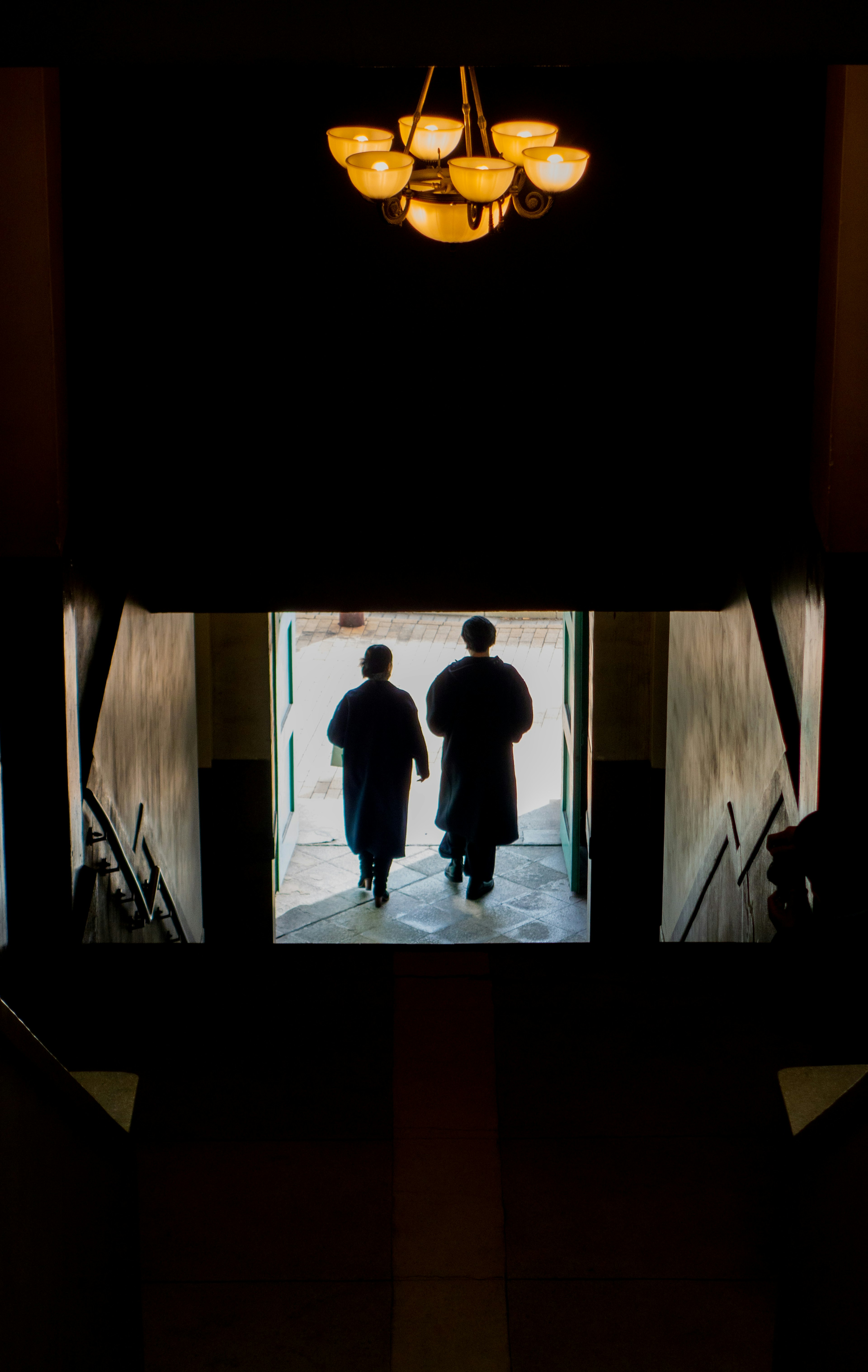 Silhouette de deux personnes descendant un escalier sous un élégant lustre