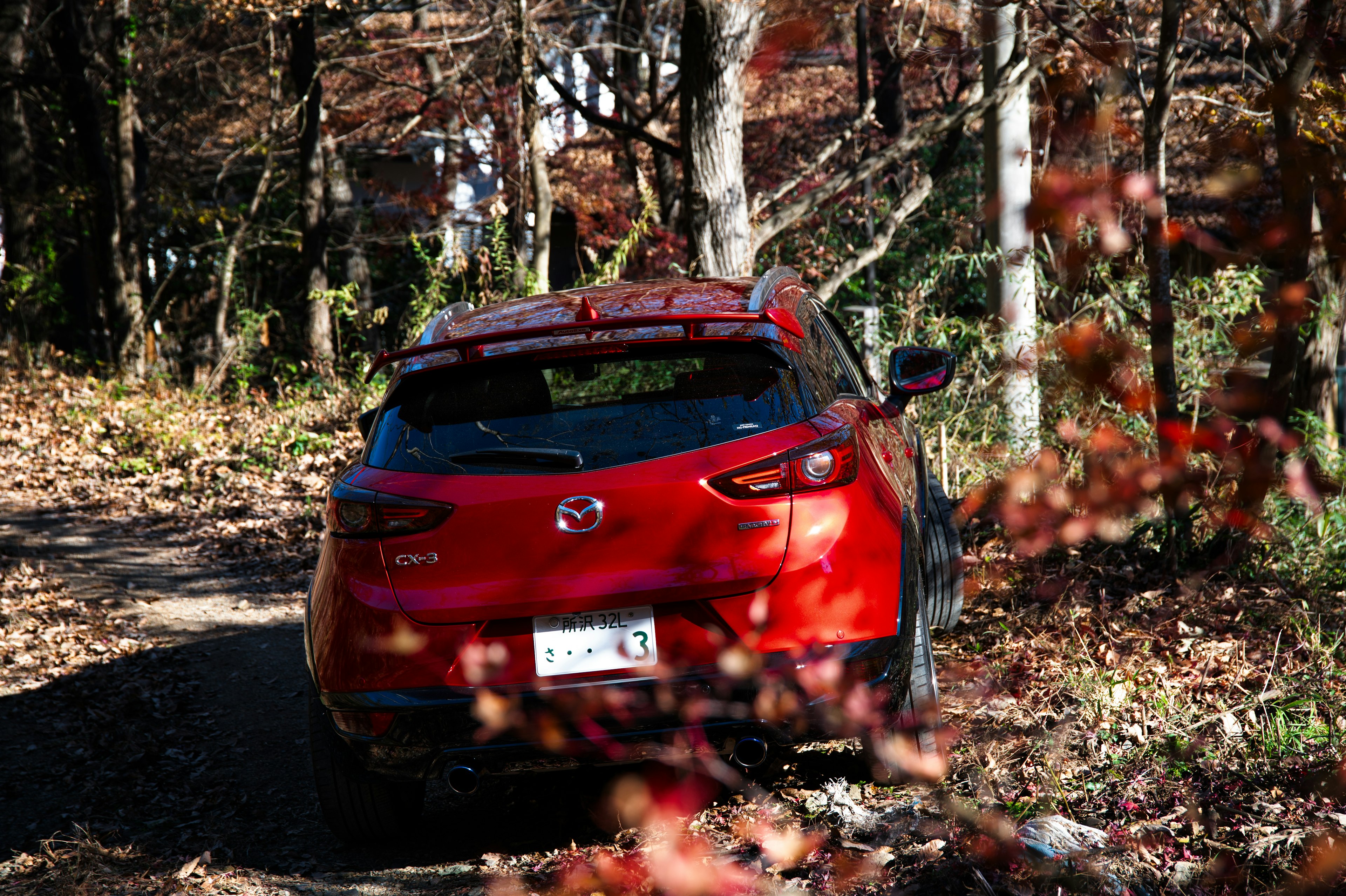 Voiture Mazda rouge garée sur un chemin forestier en automne