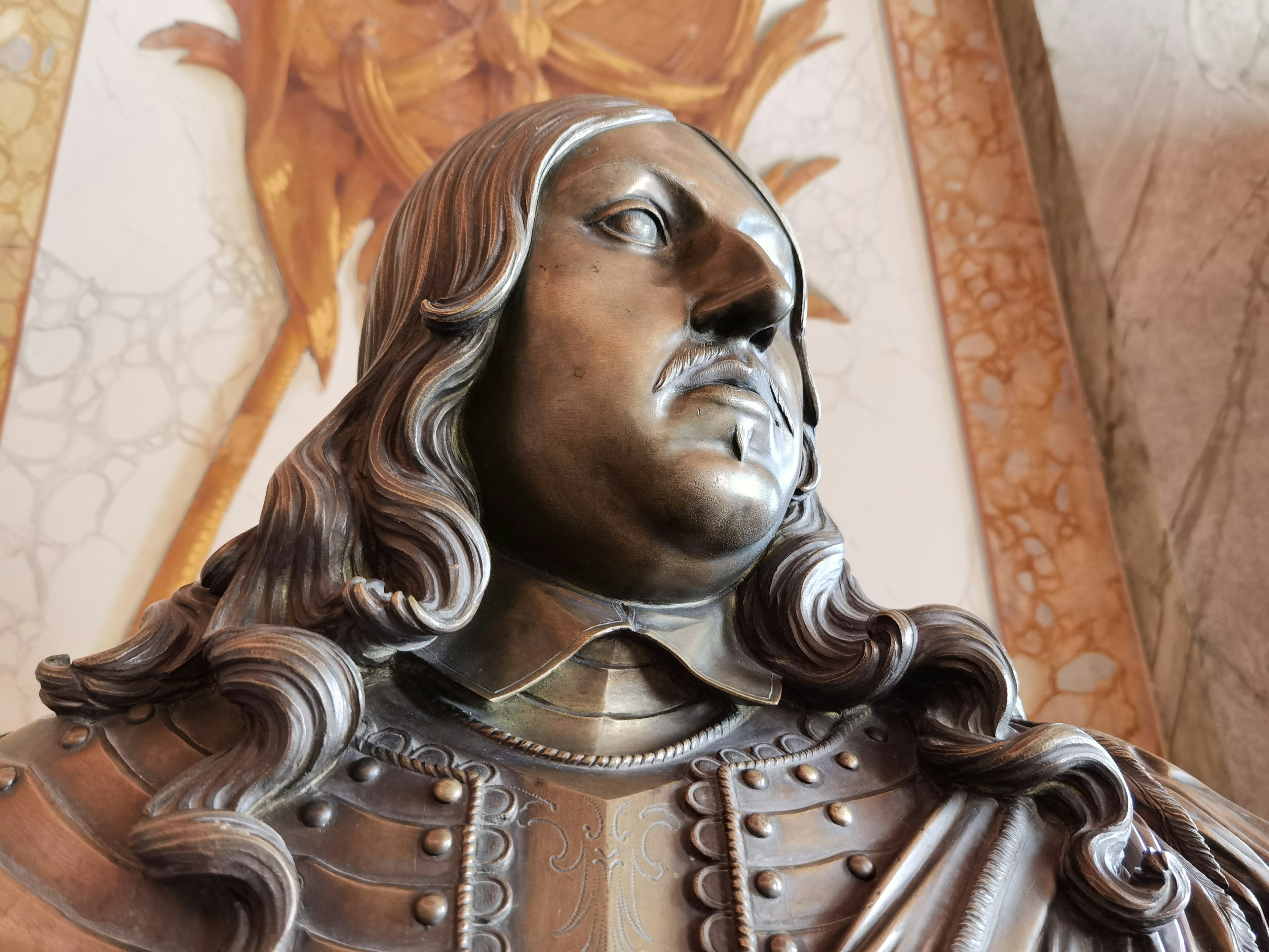 A detailed bronze bust of a historical figure with long hair and armor