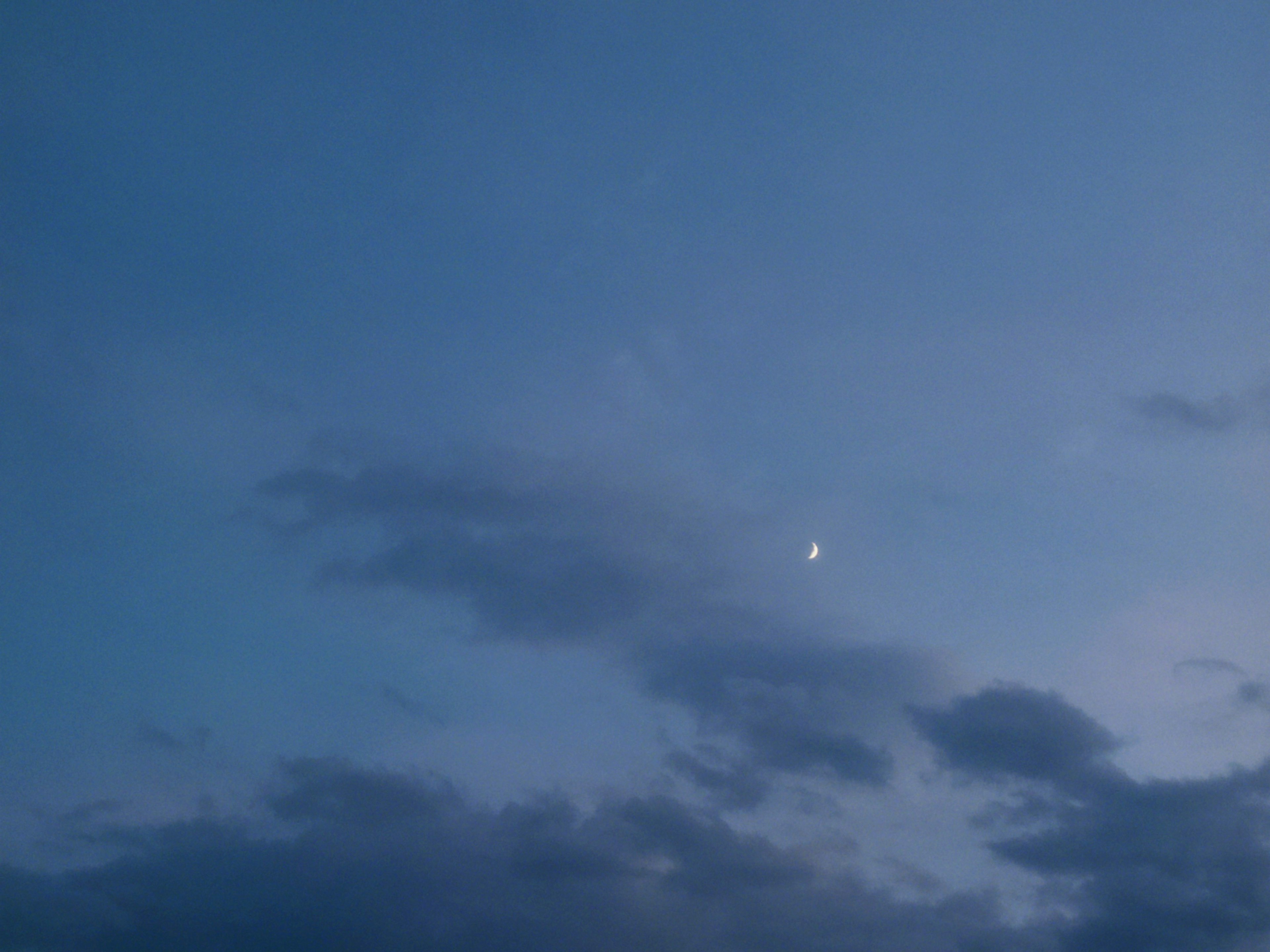 Una luna creciente brillante en un cielo azul con nubes suaves