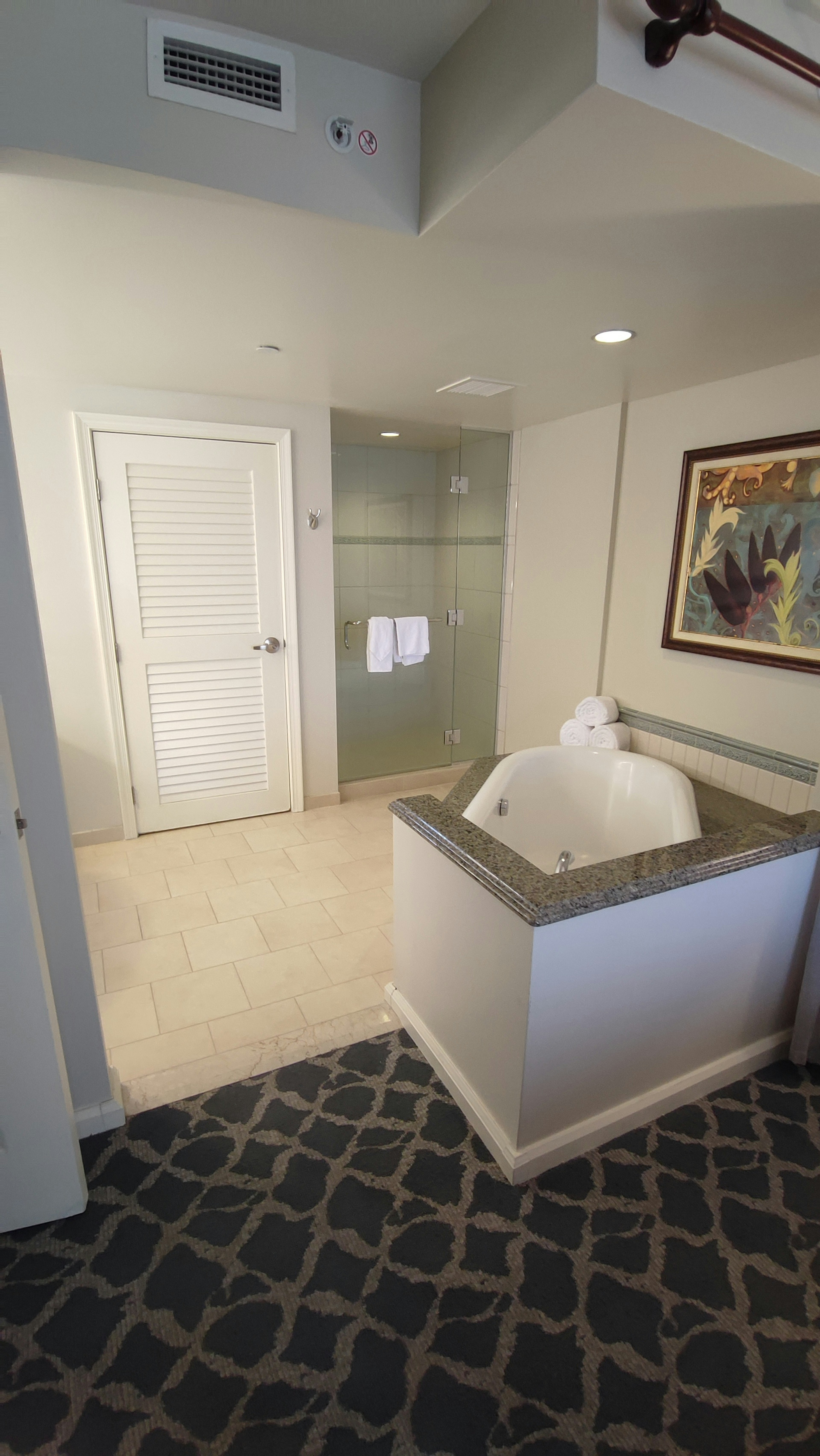 Bright bathroom interior featuring tiled floor glass shower white bathtub and wall art