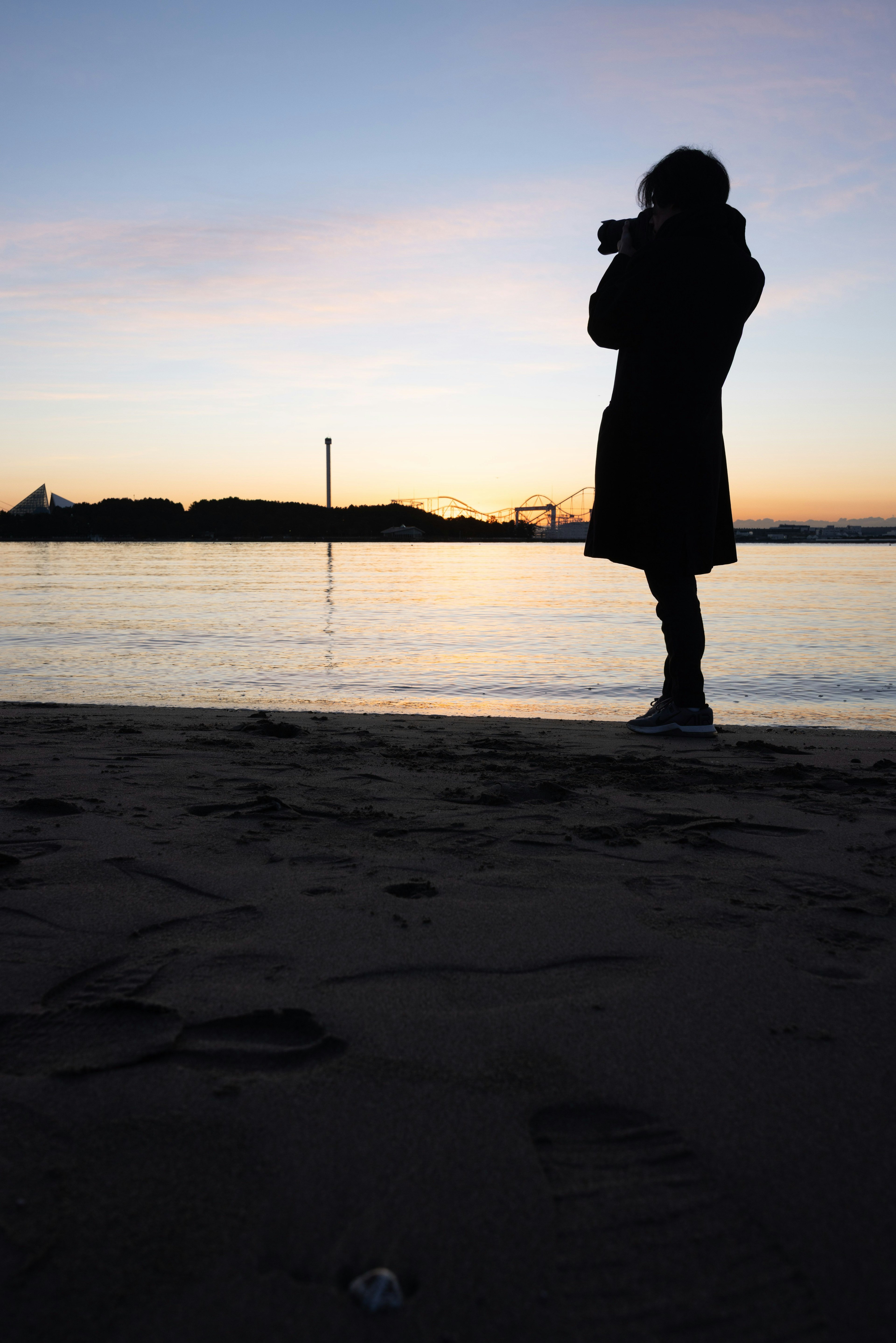 夕焼けの海辺でカメラを持つシルエットの人物