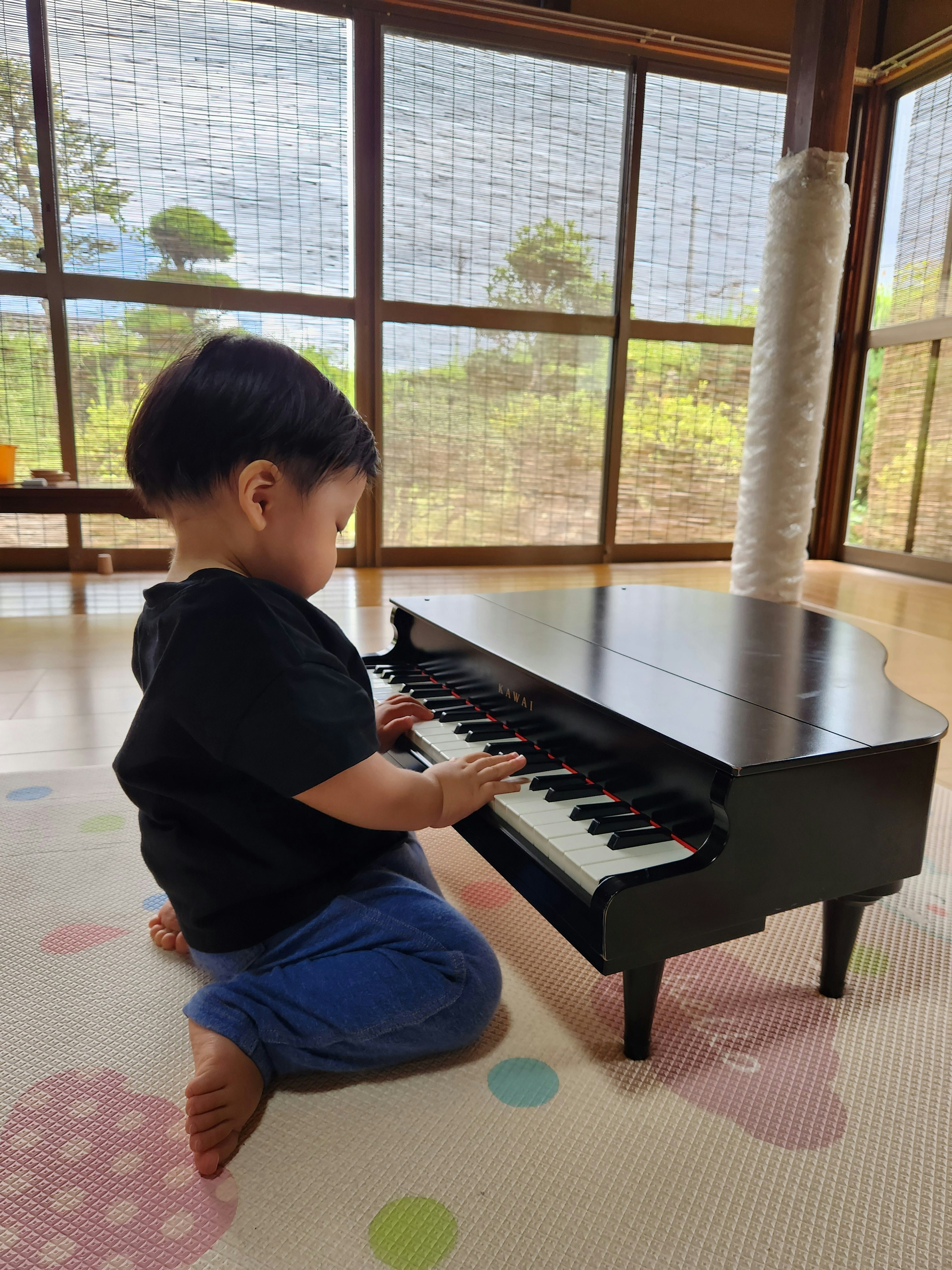 Un bambino che suona un mini pianoforte nero in uno spazio interno luminoso