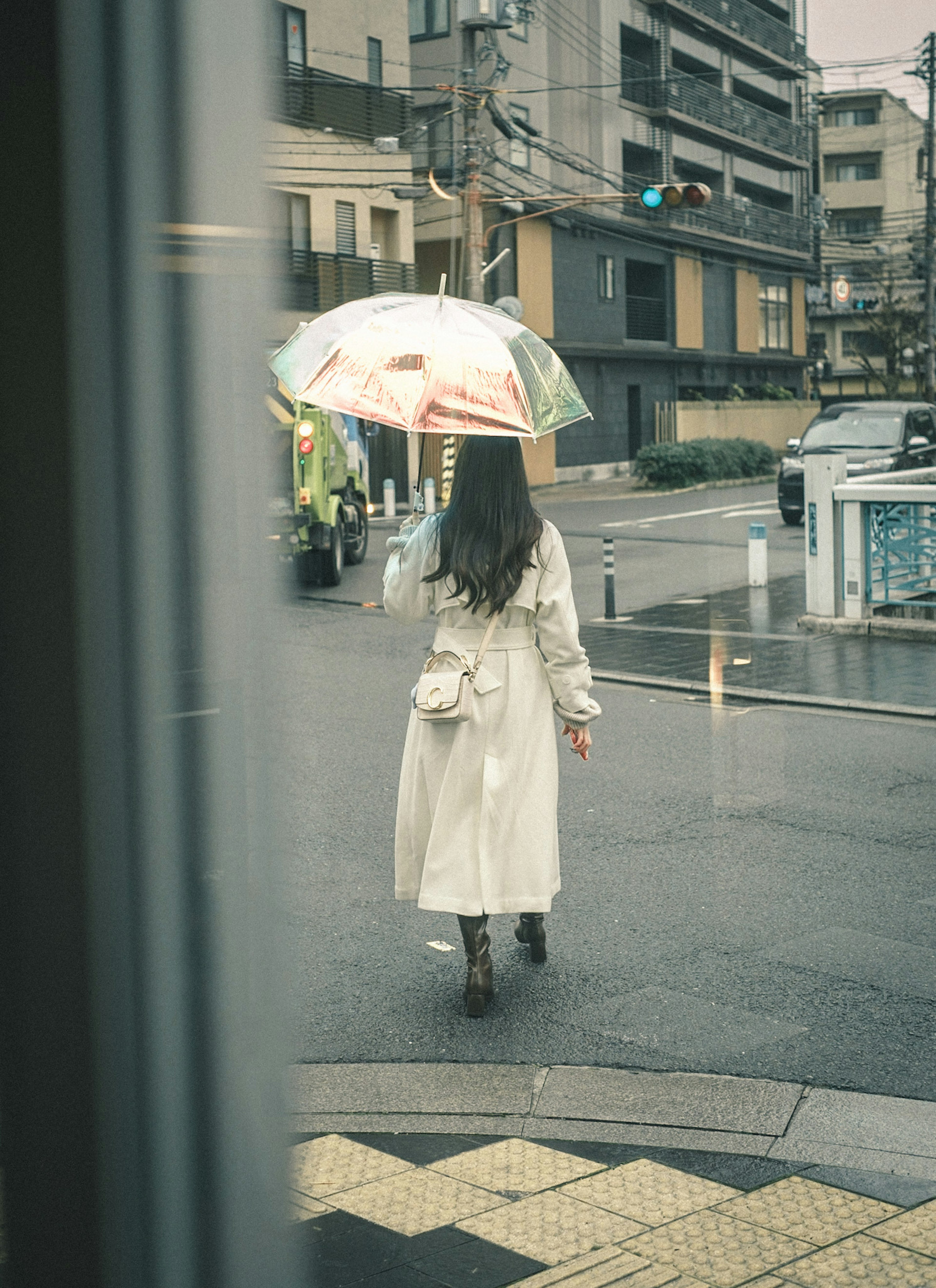 Frau, die im Regen mit einem bunten Regenschirm geht, trägt einen weißen Mantel