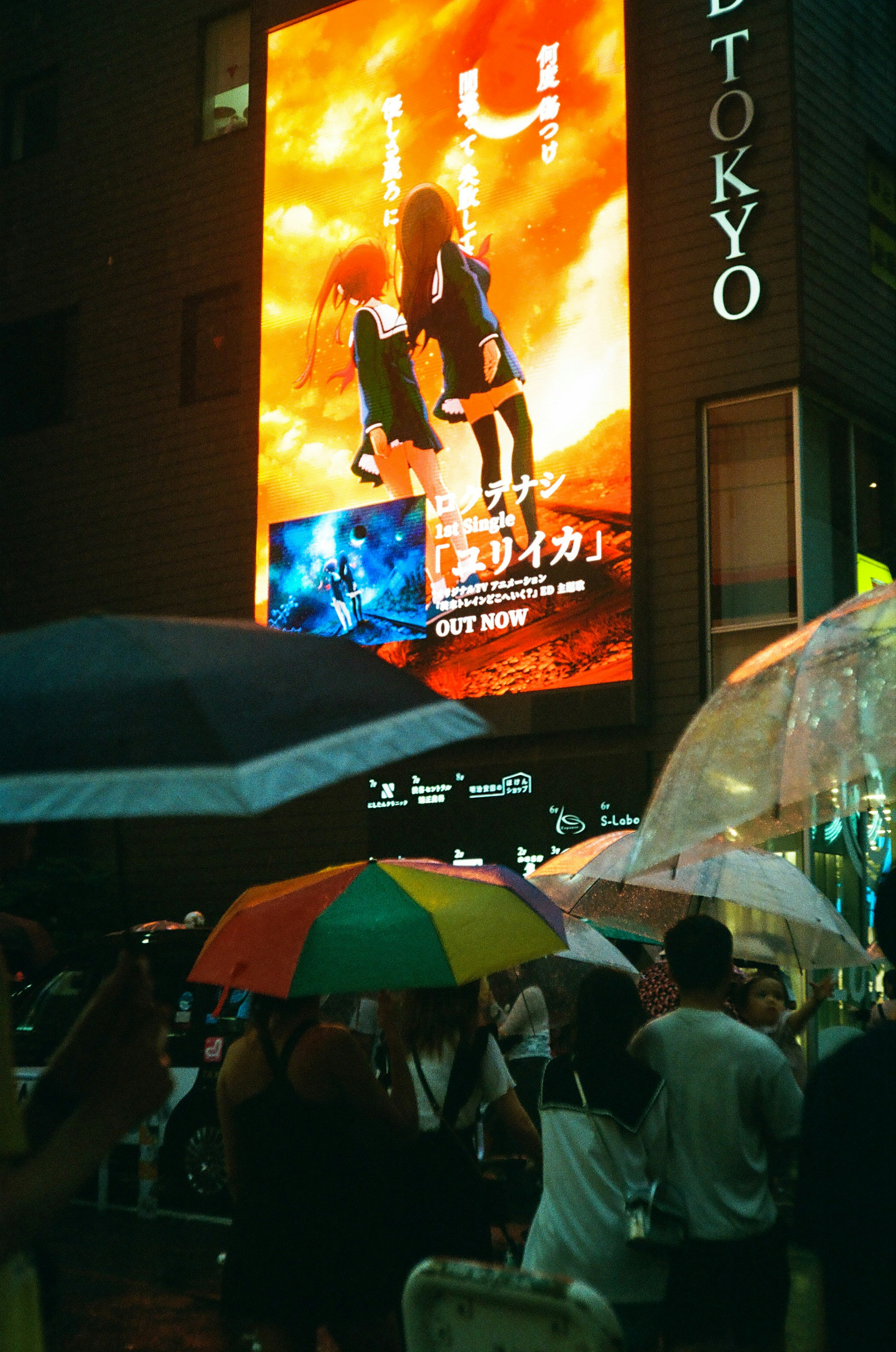 東京の街並みにある大きな広告看板と傘をさした人々