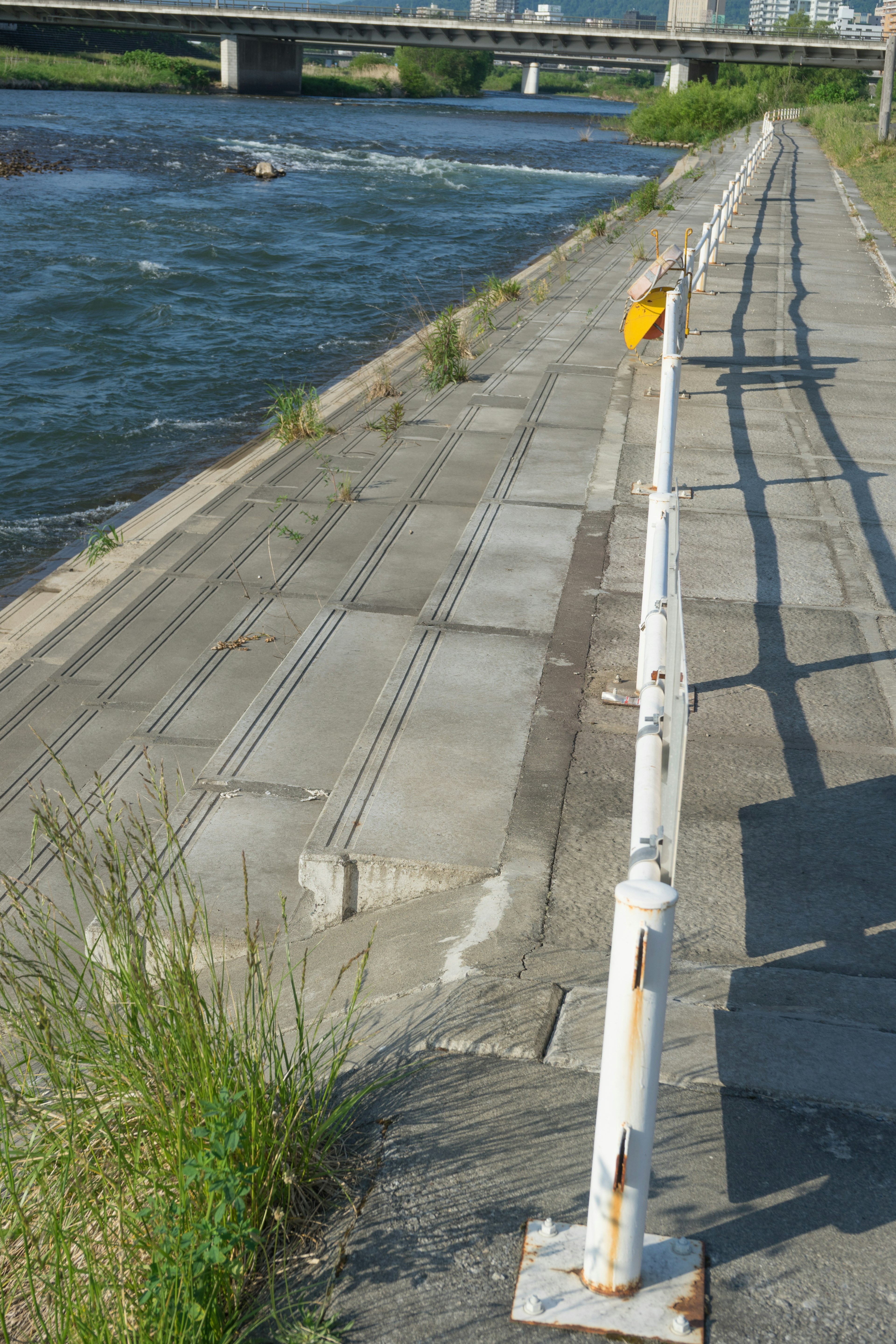 White railing along a riverbank with flowing water and green grass