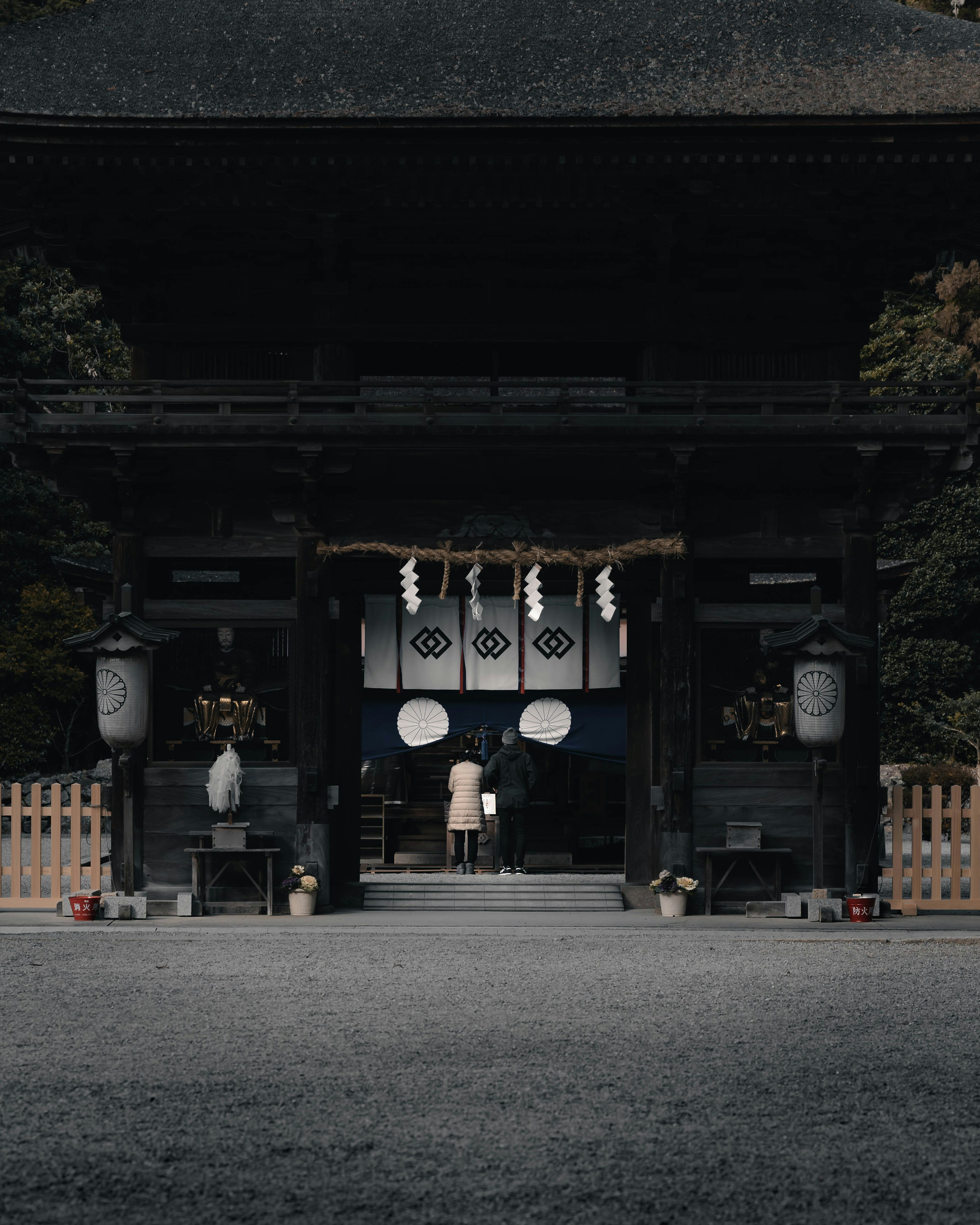 A person standing at the entrance of a shrine with traditional decorations on the gate