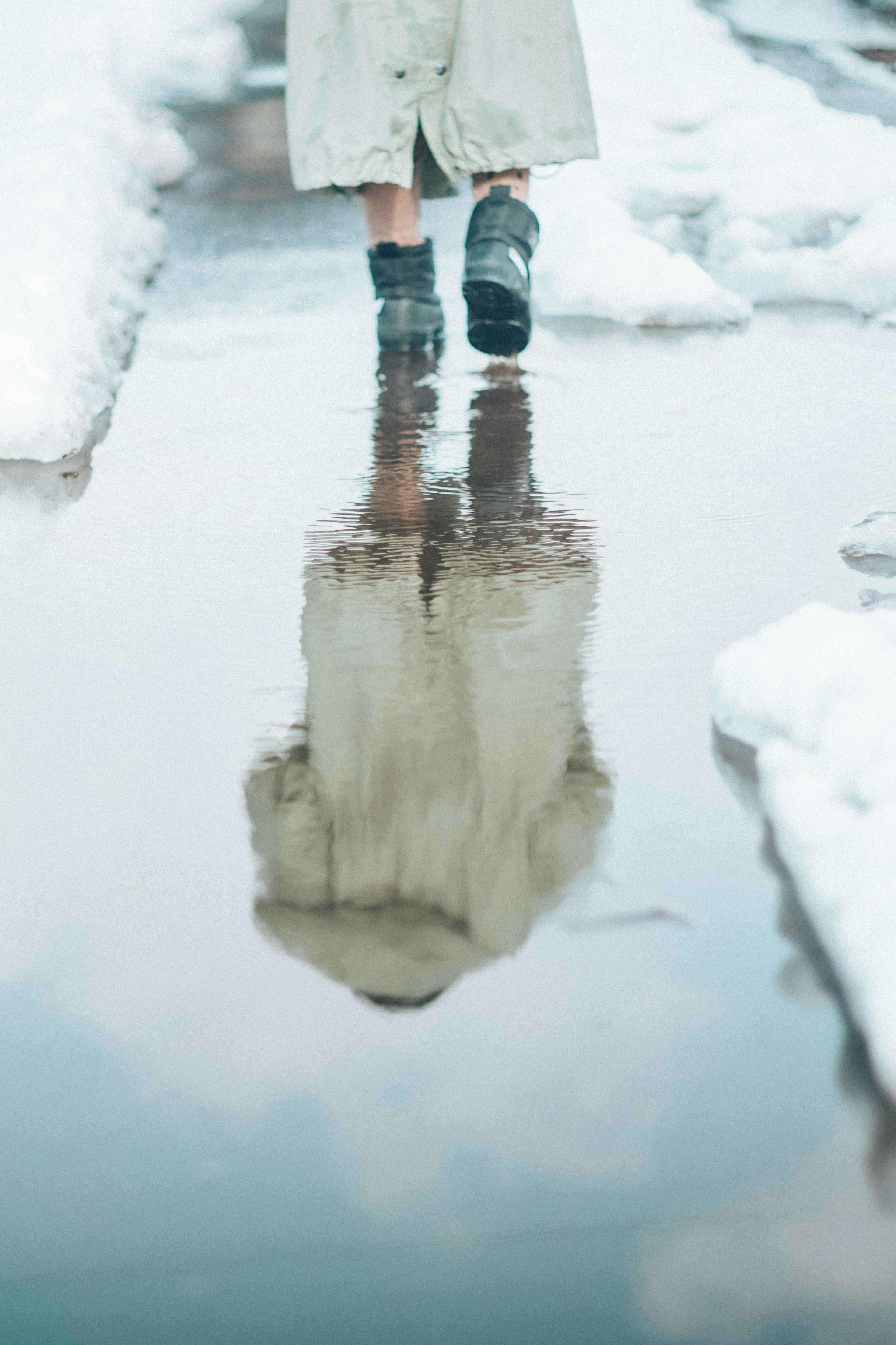 一个人在雪中行走时，倒影在水洼里