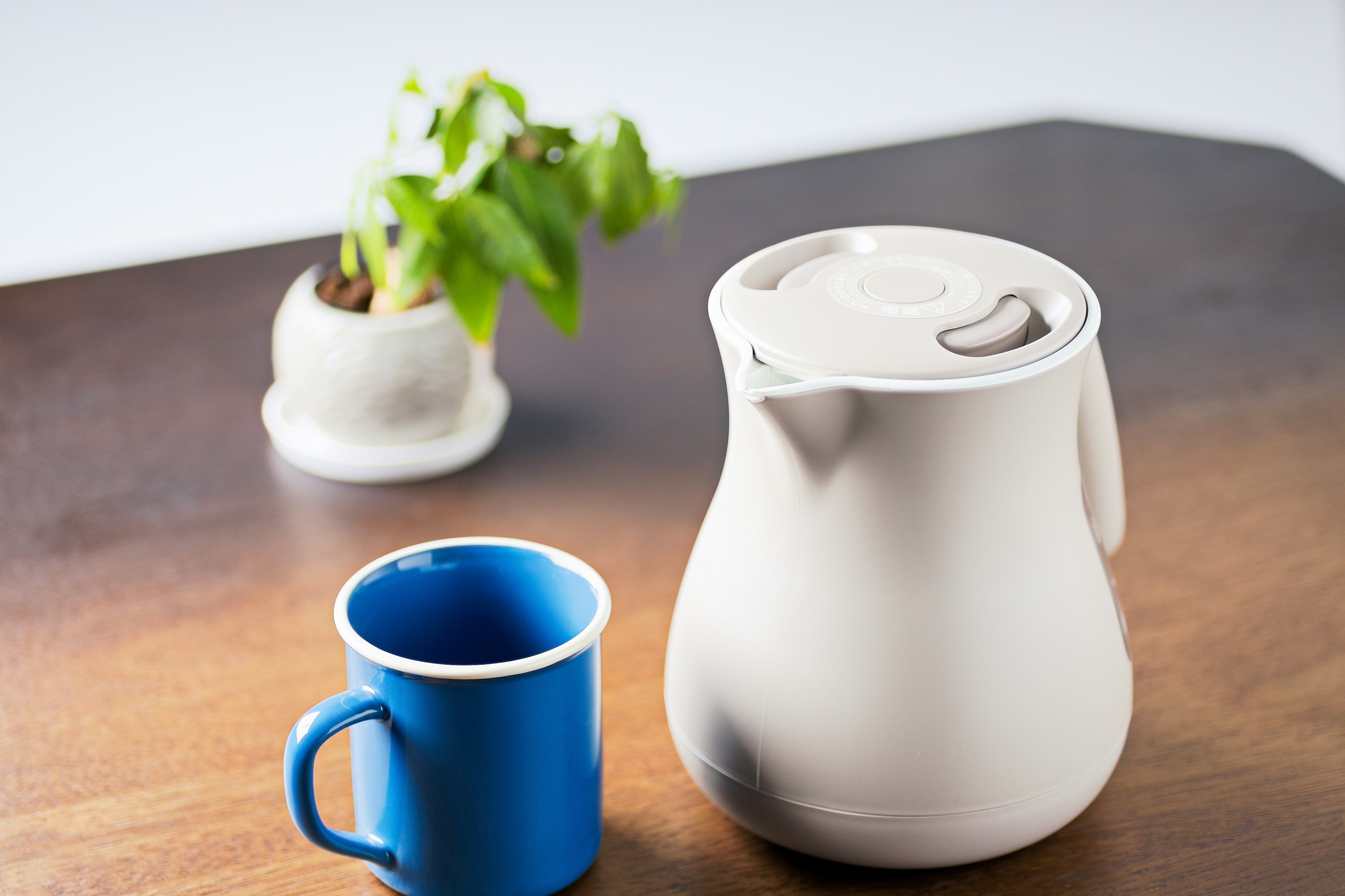 Une scène simple avec une carafe blanche et une tasse bleue sur une table en bois