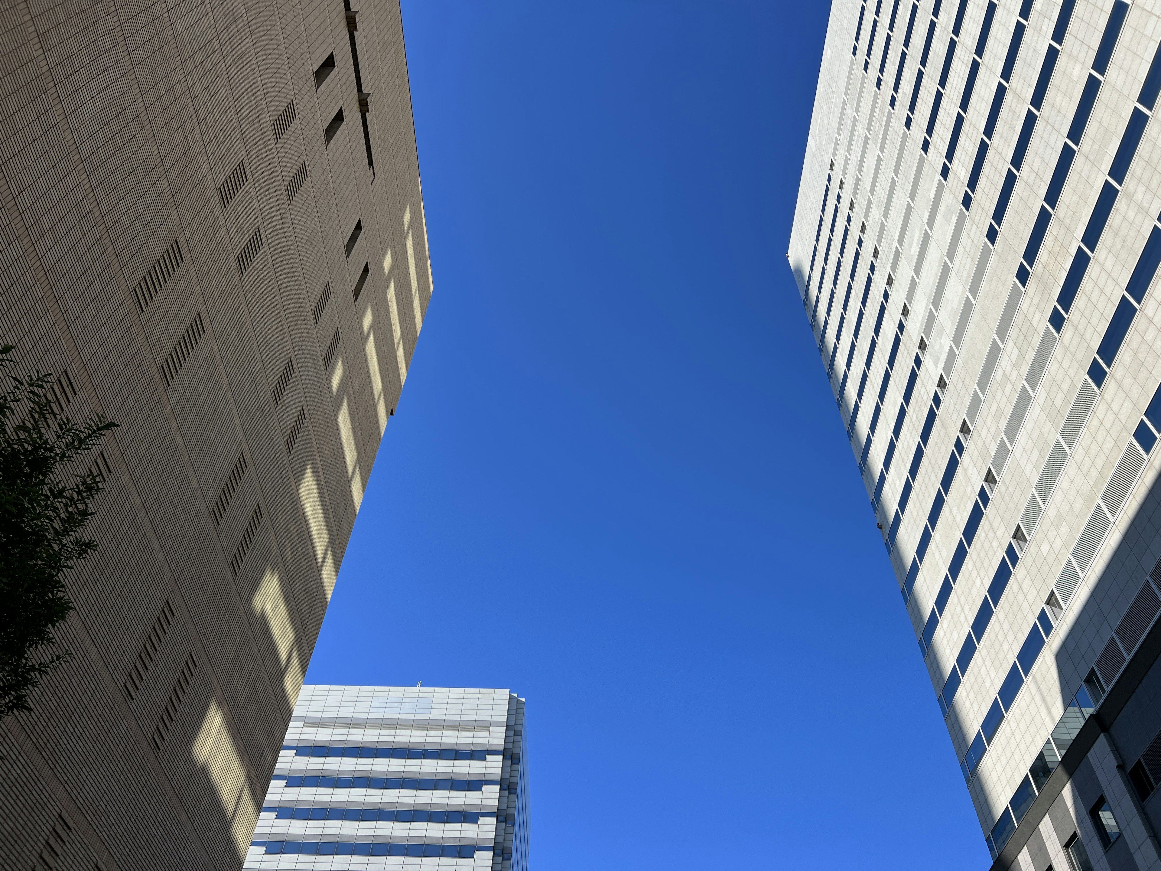 View looking up between tall buildings against a clear blue sky